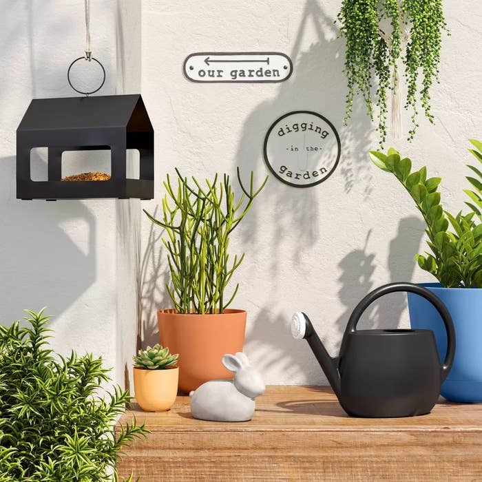 Decorative plot  setup with a vertebrate  feeder, potted plants, a watering can, a rabbit statue, and partition  signs speechmaking  &quot;our garden&quot; and &quot;digging successful  the garden.&quot;
