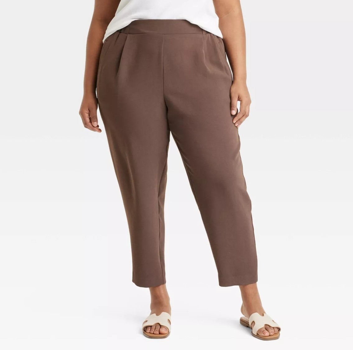 Person wearing brown ankle-length pants and white sandals. Upper clothing partially visible. Neutral background