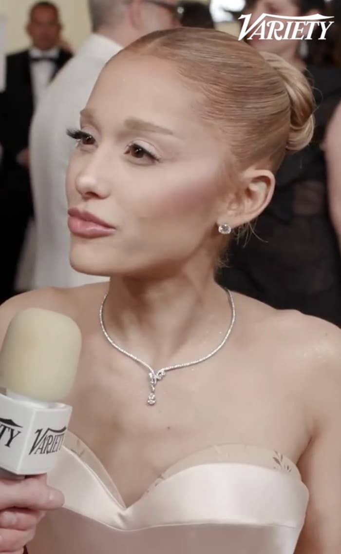 Person in elegant gown with a diamond necklace speaks into a microphone at a formal event