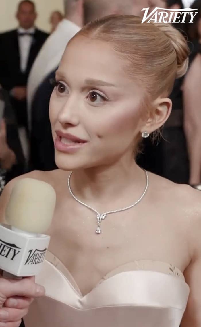 Person on a red carpet in an elegant dress, being interviewed with a microphone marked