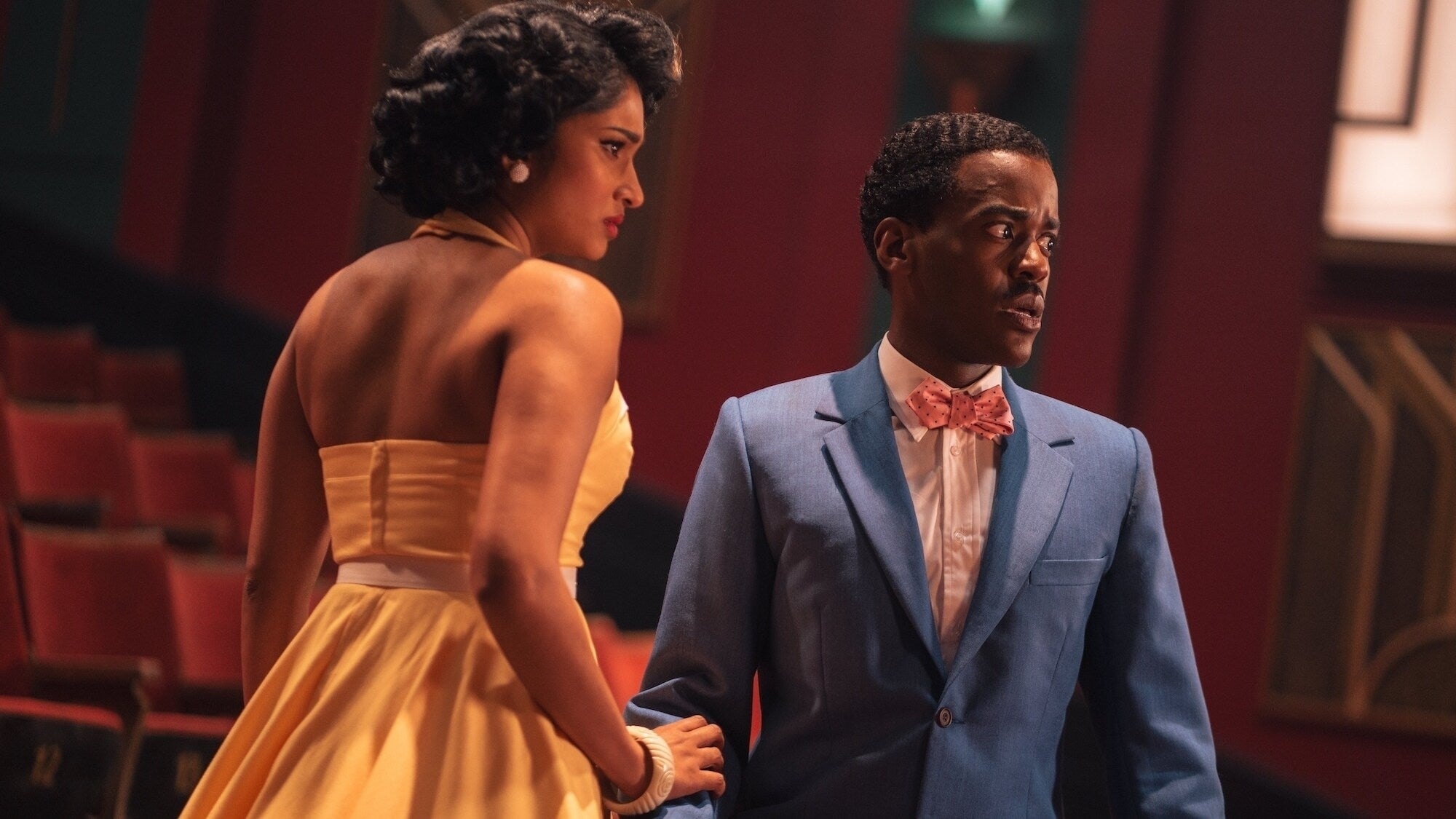 The Doctor and Belinda standing on a stage in vintage clothing in a scene from "Doctor Who"