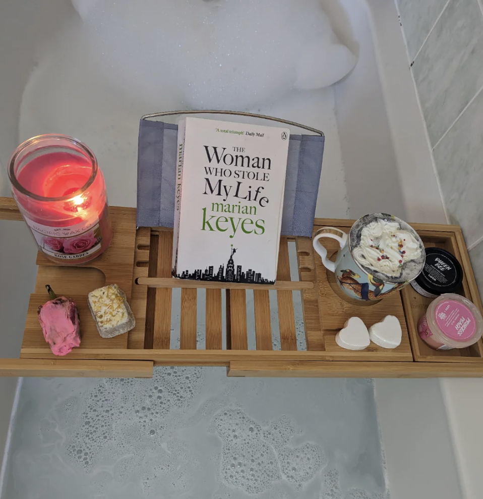 Et badebrett har et opplyst stearinlys, bok og frodige kosmetikkprodukter ved siden av et badekar