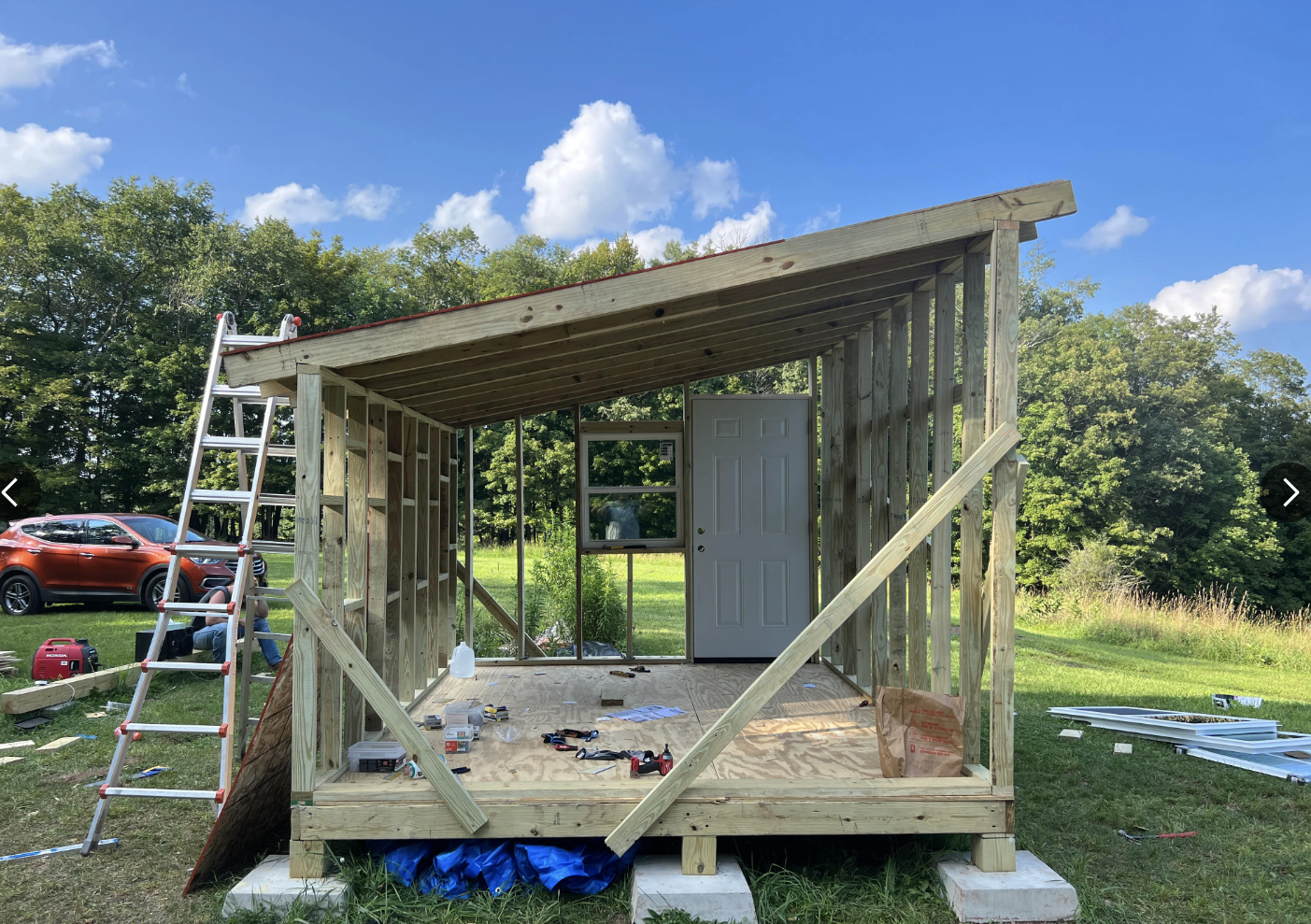 Et delvis konstruert bittesmå hjem med innramming og vinduer på et gresskledd område, som viser DIY -fremgang. Brukere ' Reddit -kommentarer vises rundt det