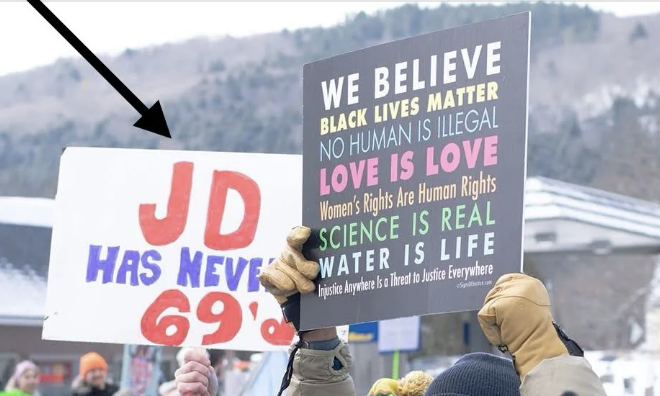 Protesters holding signs with messages astir  rights; 1  motion   starts with "JD has never" and different  features assorted  societal  justness  statements