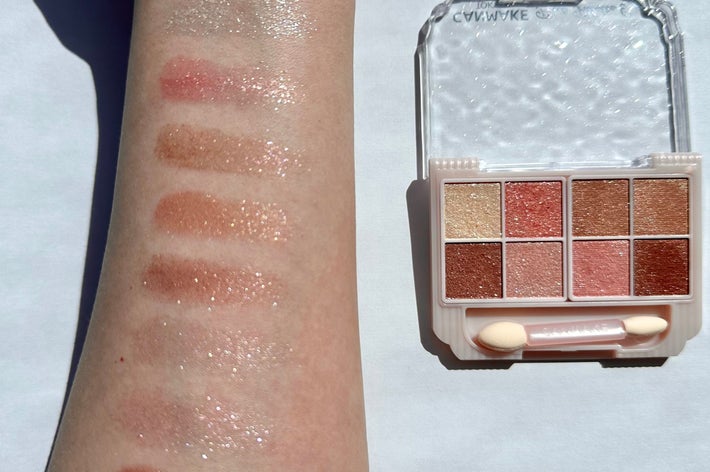 腕に塗られたアイシャドウの色見本。隣に9色のアイシャドウパレットがあり、ピンク系の色合いが並んでいる。