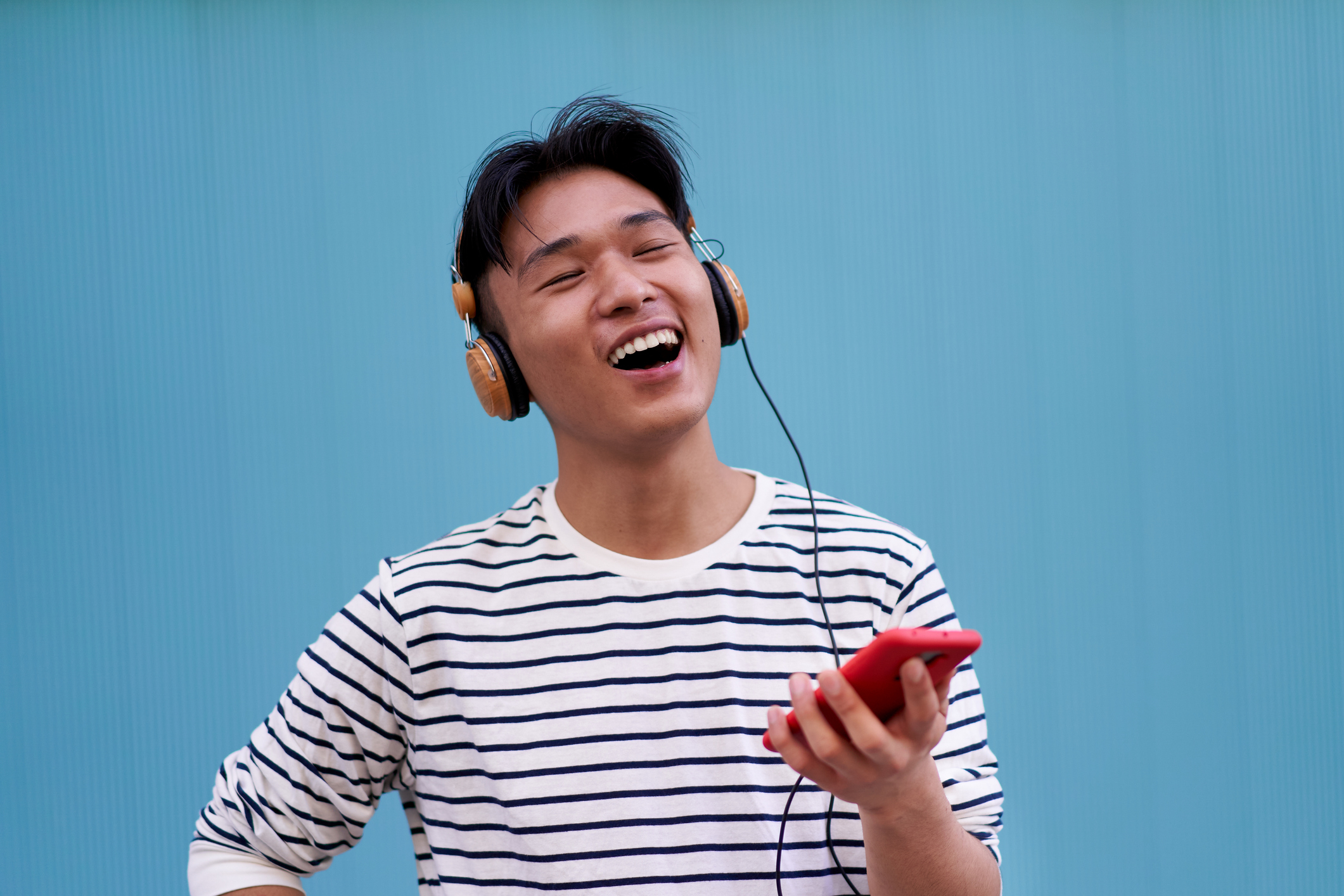 Person som har hodetelefoner, smiler og holder en smarttelefon. De ser ut til å glede seg over musikk, og står mot en vanlig bakgrunn