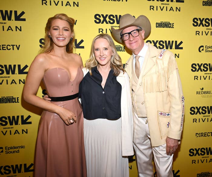 Three people pose together at a SXSW event; one in a strapless dress, another in a blouse and jacket, and the third in a suit and cowboy hat