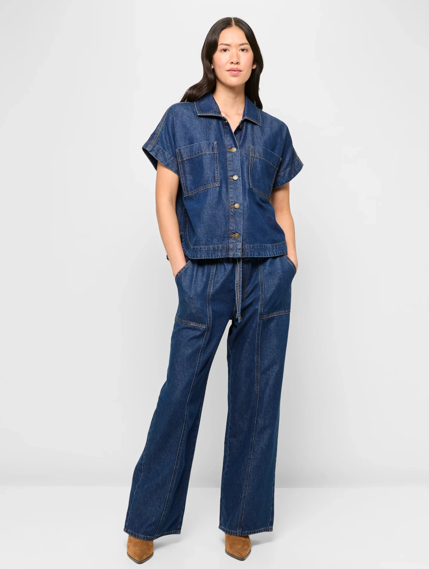 Person in a denim jumpsuit with short sleeves and wide legs, posing confidently with hands in pockets