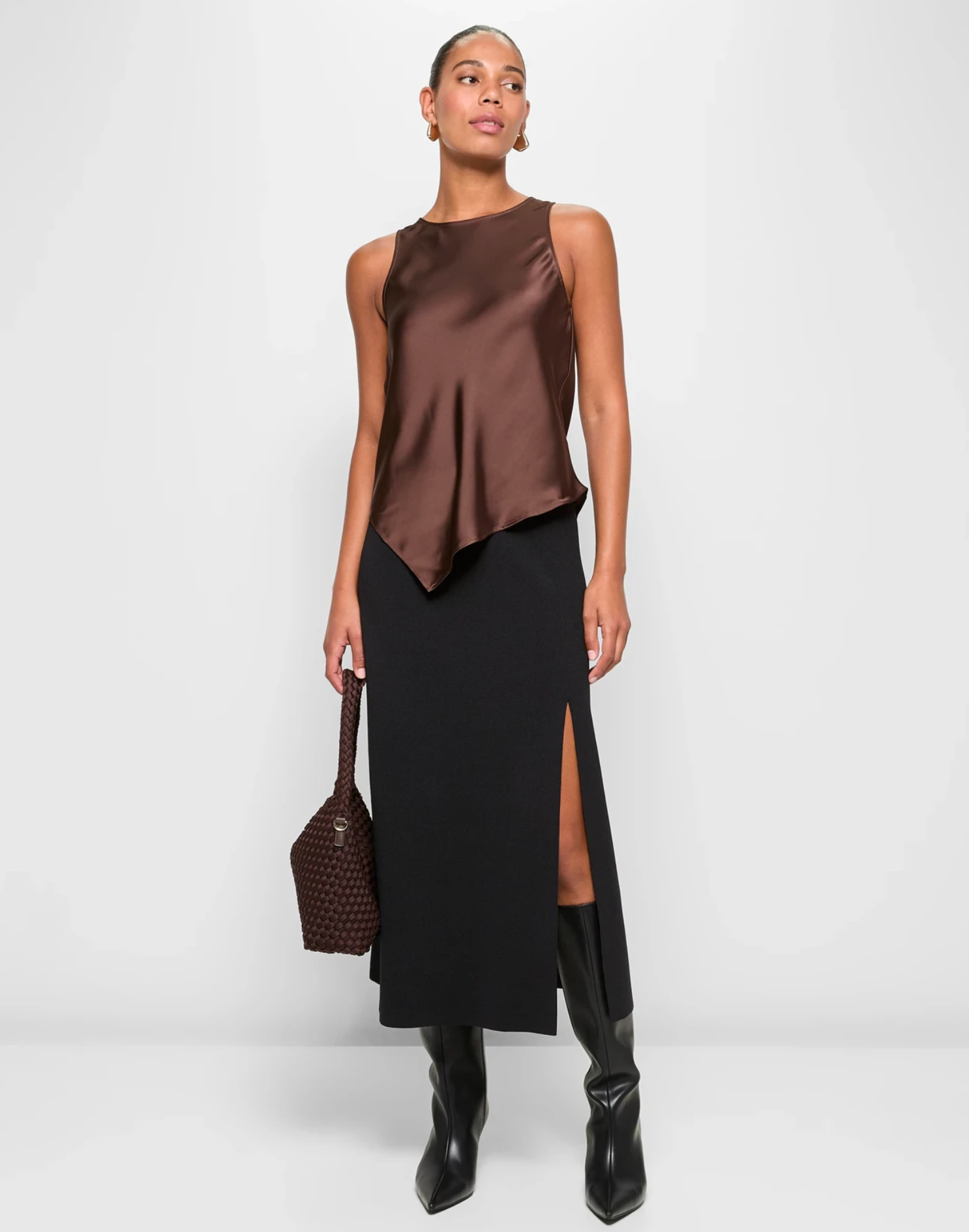 Person wearing a sleeveless, asymmetrical top and a long skirt with a side slit, holding a textured bag