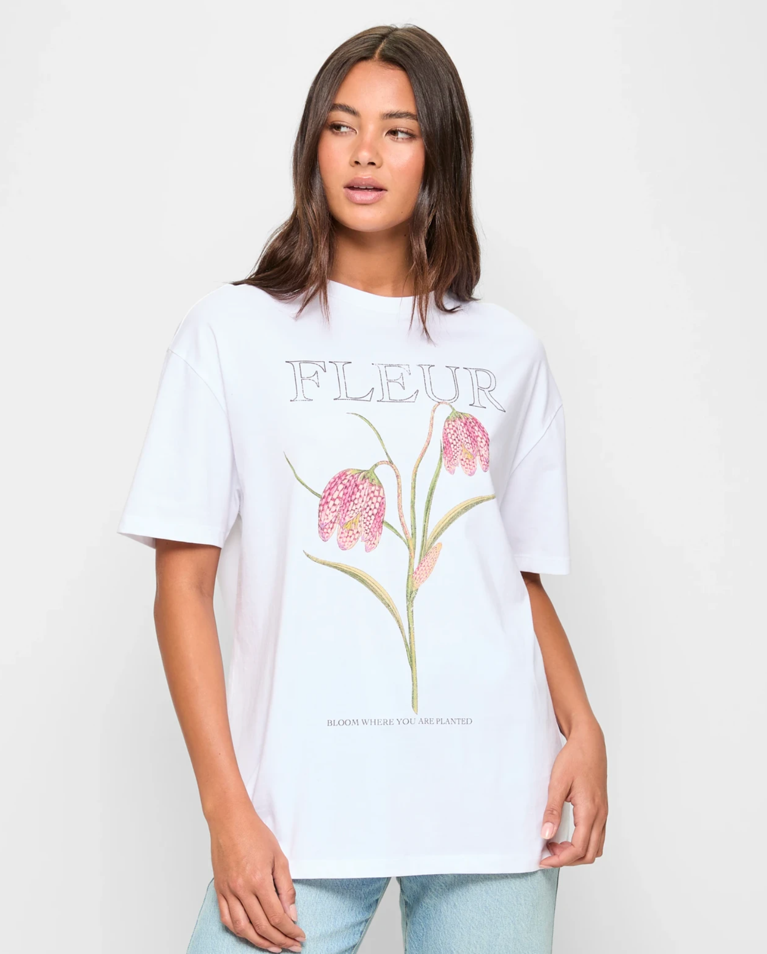 Person wearing a white T-shirt with floral illustration and "FLEUR" text, paired with jeans