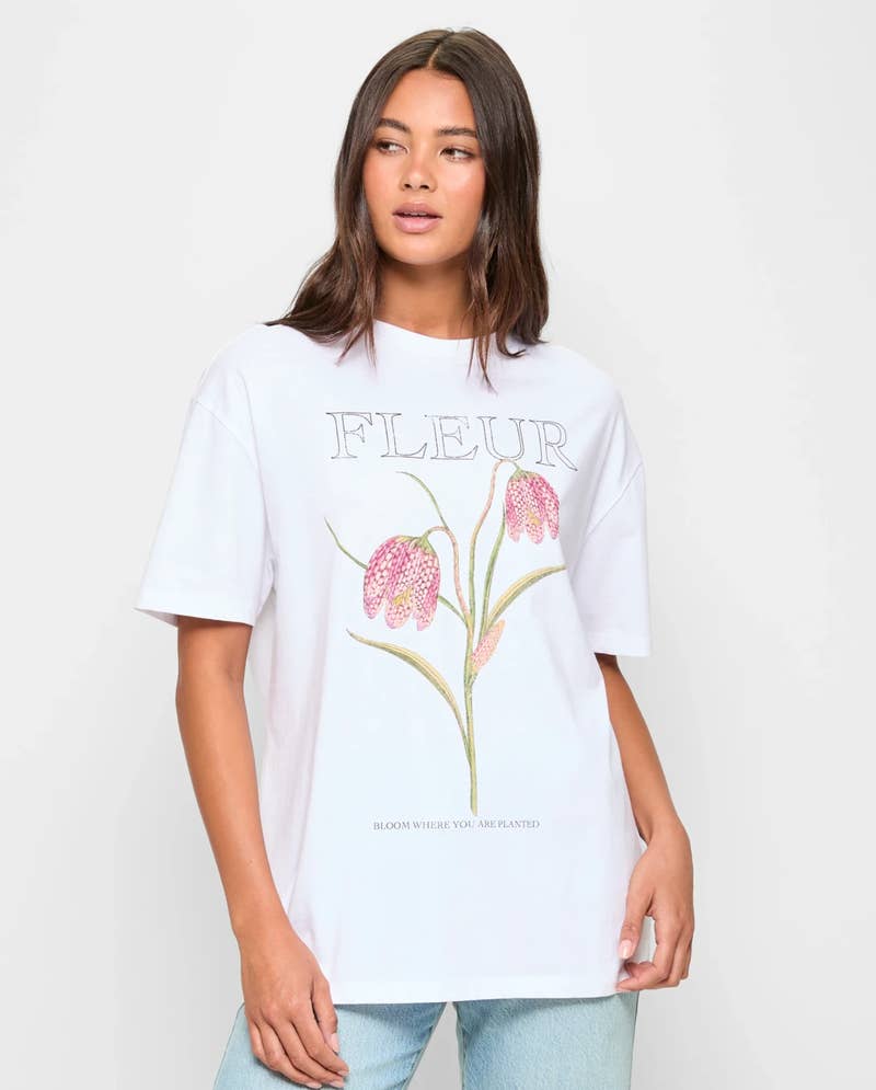 Person wearing a white T-shirt with floral illustration and "FLEUR" text, paired with jeans