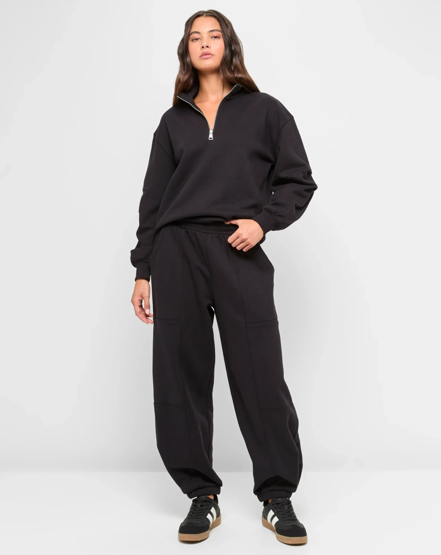 Person wearing relaxed-fit tracksuit and sneakers, standing confidently against a plain backdrop