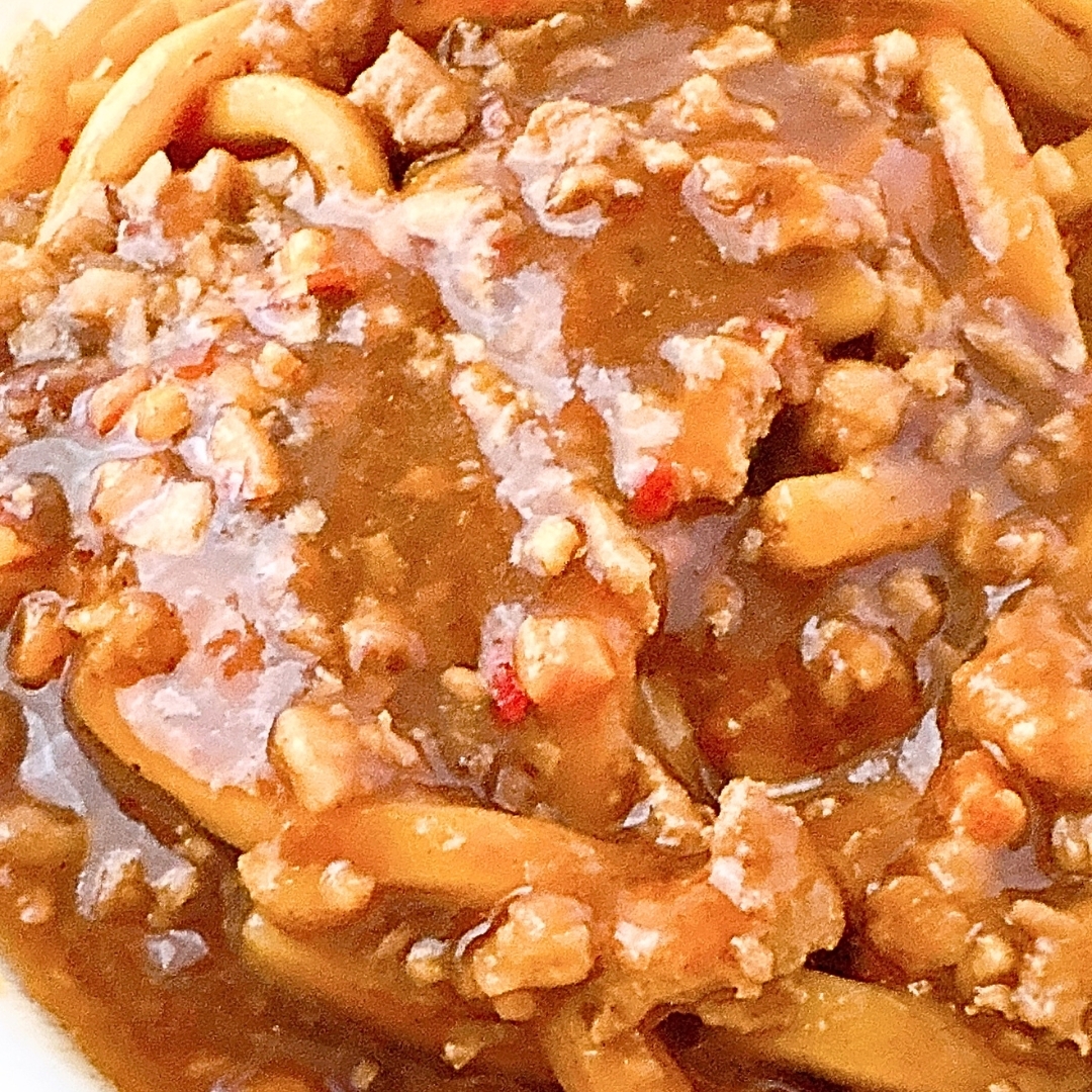 麺にたっぷりと肉やソースがかかった料理のクローズアップ。