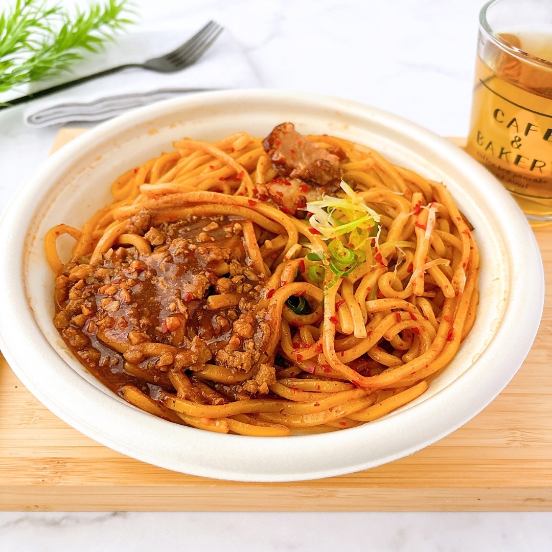 うどんボウルには、肉とスパイシーなソースがたっぷりかかっています。横にカフェ＆ベーカリーのドリンクがあります。