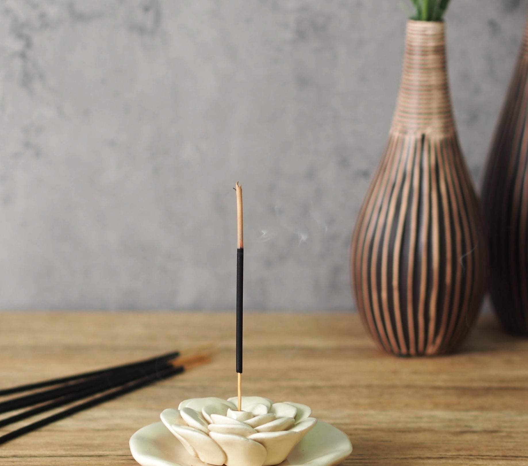 Incense sticks displayed with a lit stick in a floral holder in beige