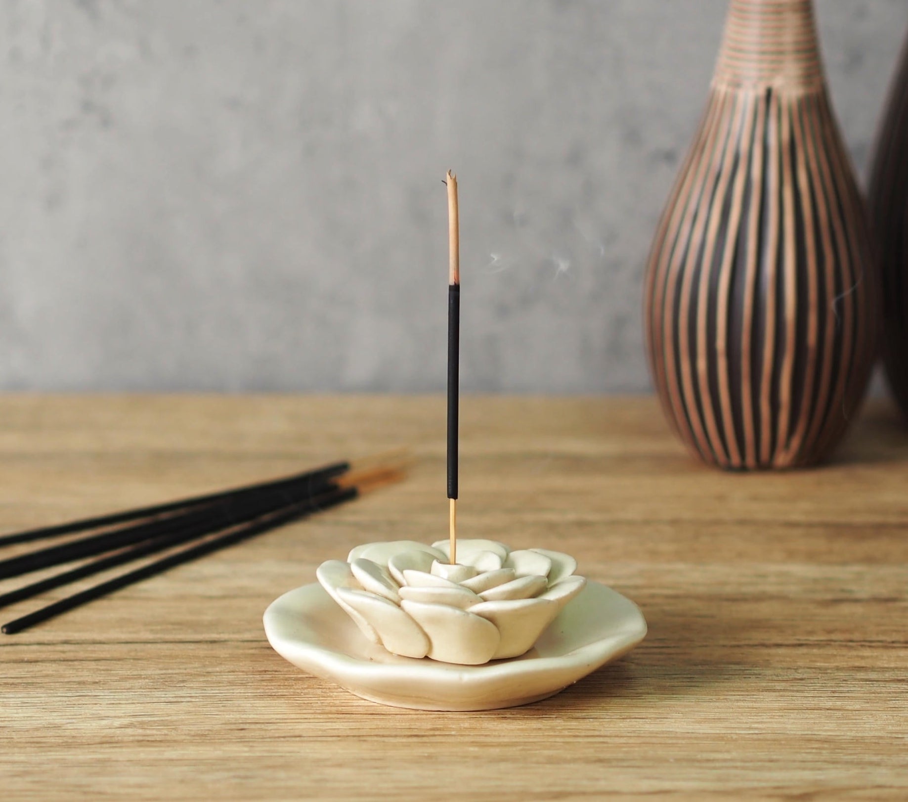 Incense sticks displayed with a lit stick in a floral holder in beige