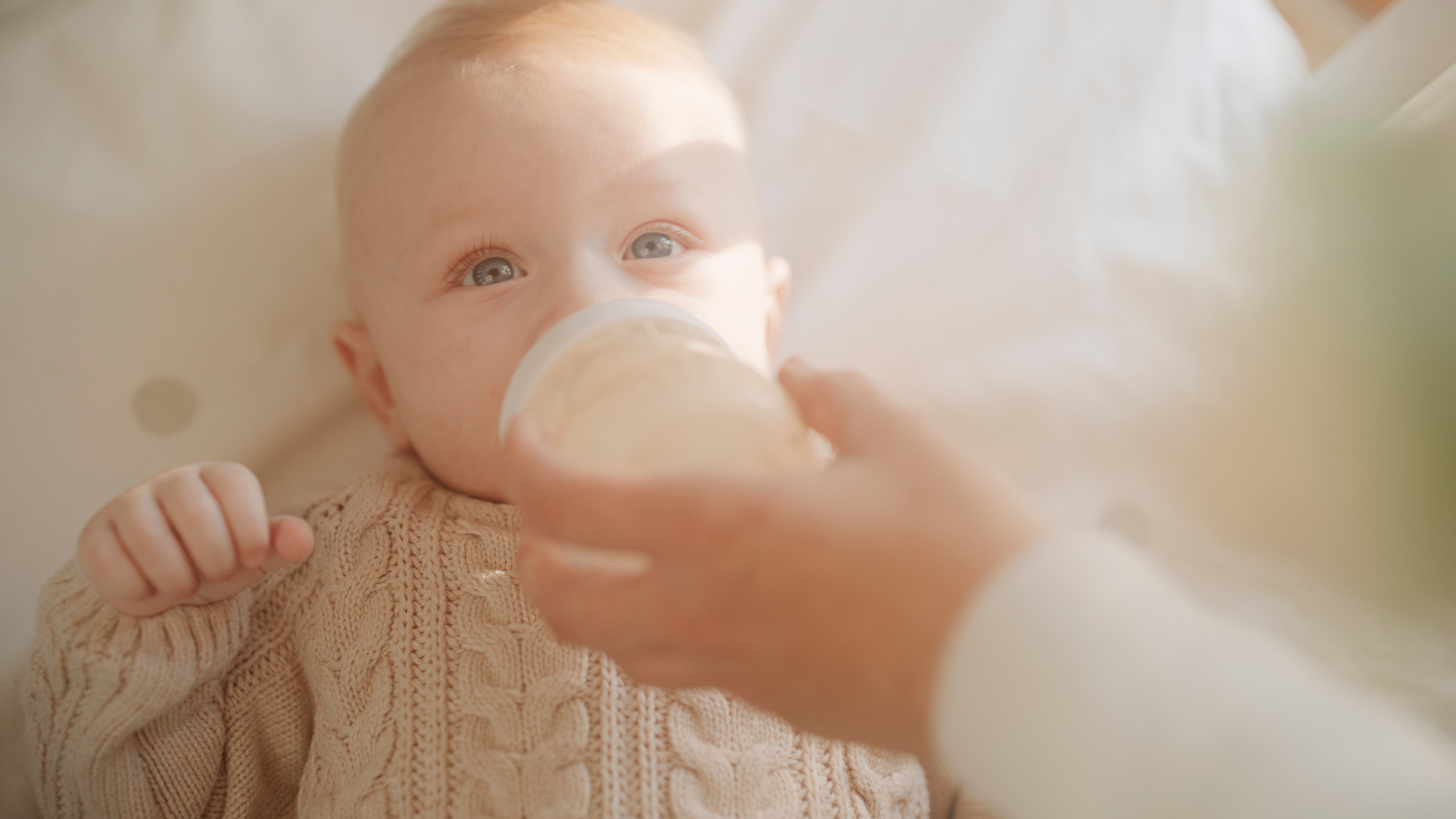 Baby in cozy sweater being bottle-fed while lying down