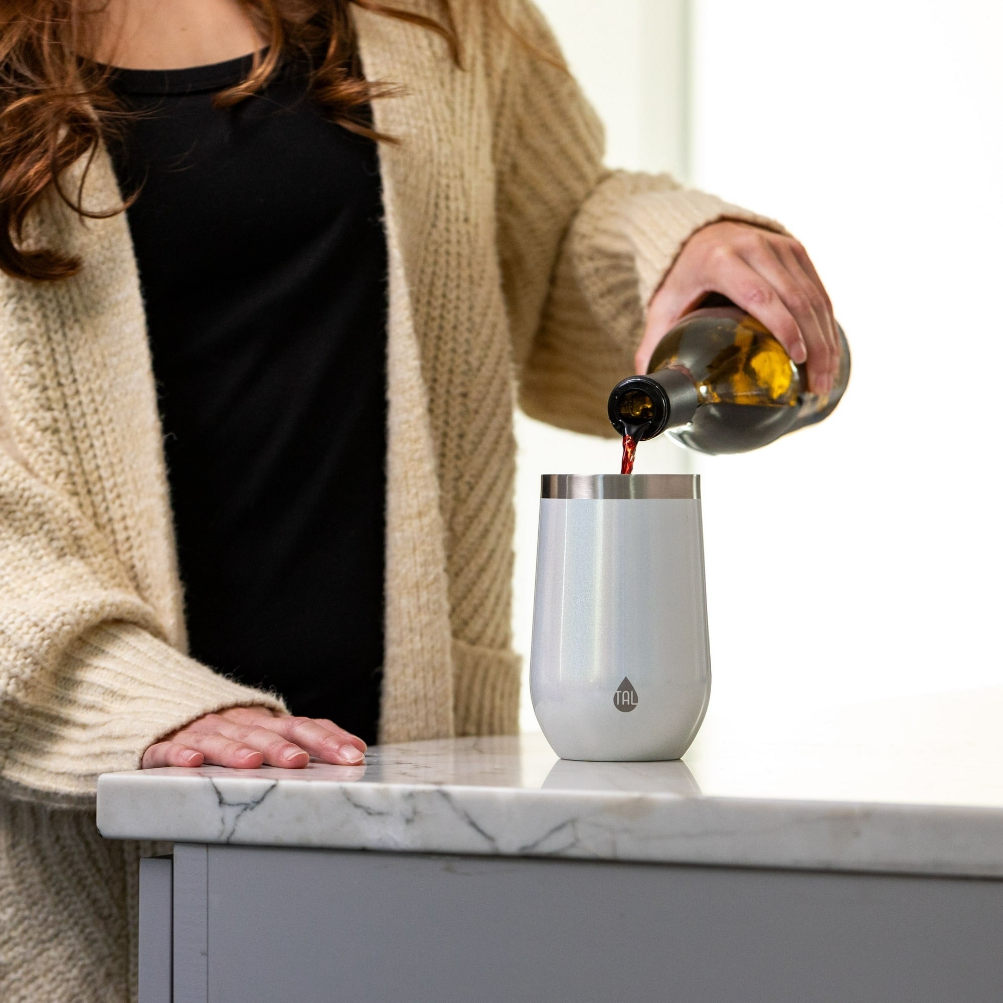 Person pouring beverage into a white iridescent stainless steel tumbler on a kitchen counter