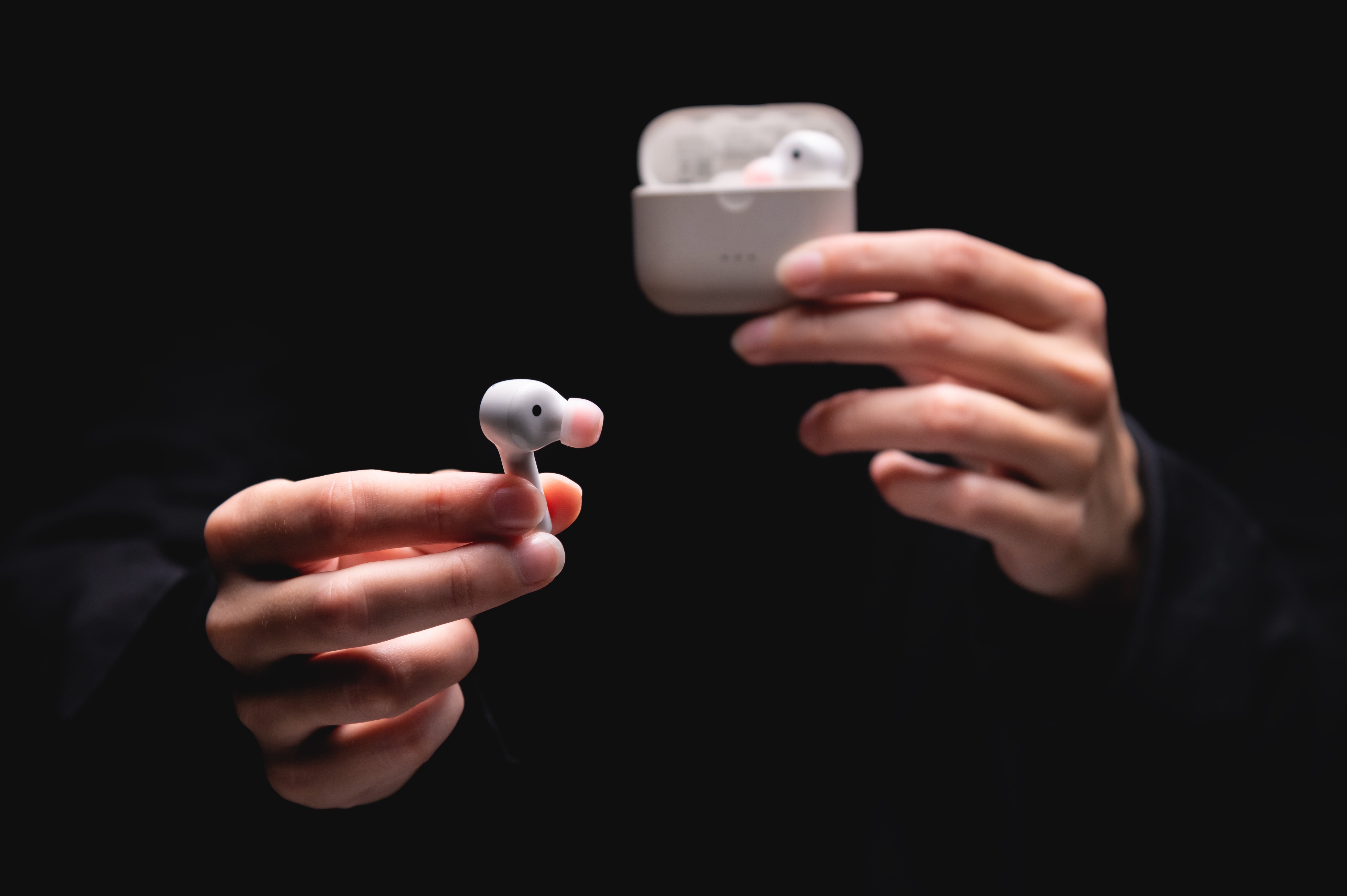Hands holding AirPods against a black background