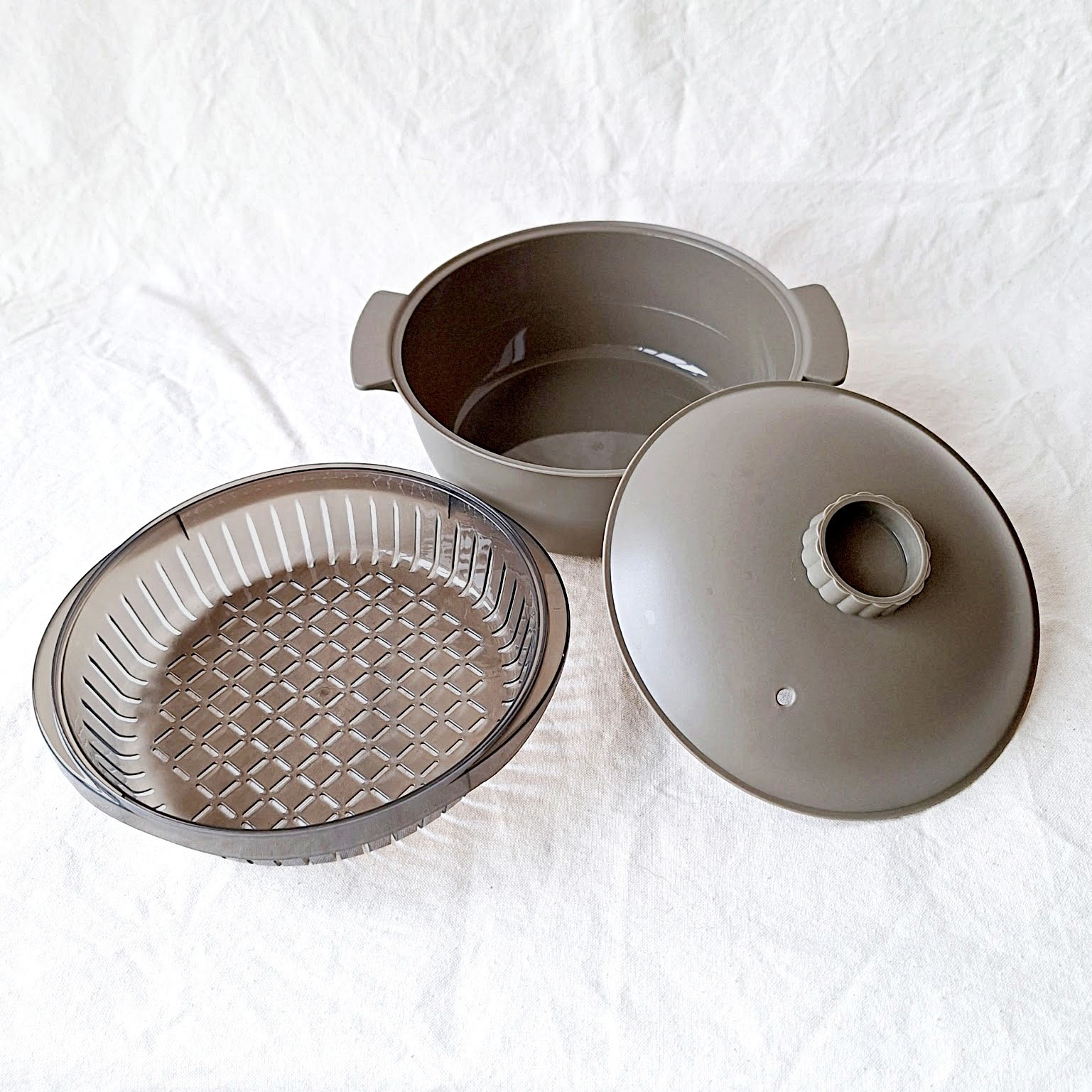 3つのパーツからなる調理器具セット。鍋、蒸し器、フタが置かれている。シンプルで機能的なデザイン。
