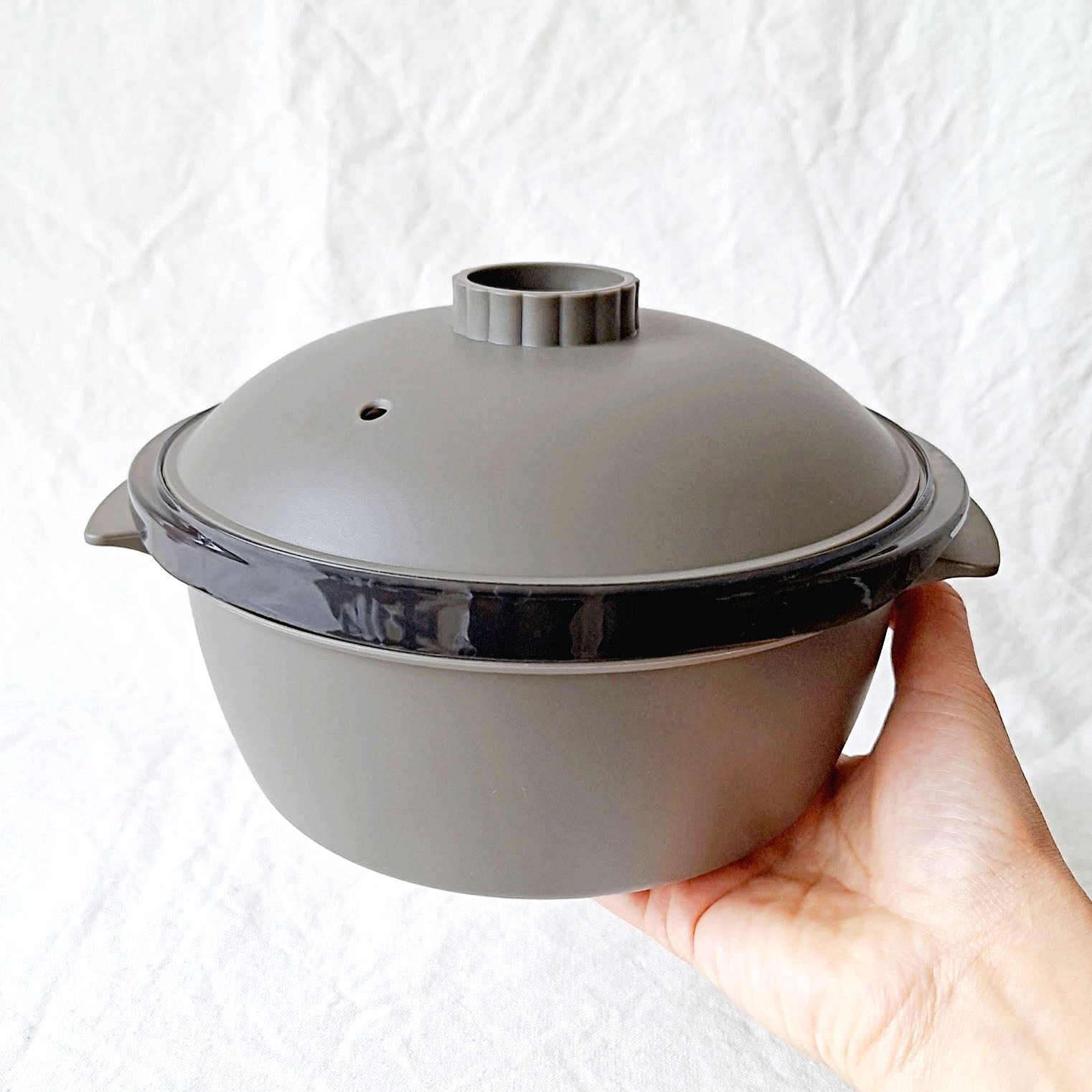 手に持たれた蓋付きの調理用鍋。シンプルなデザインが特徴。