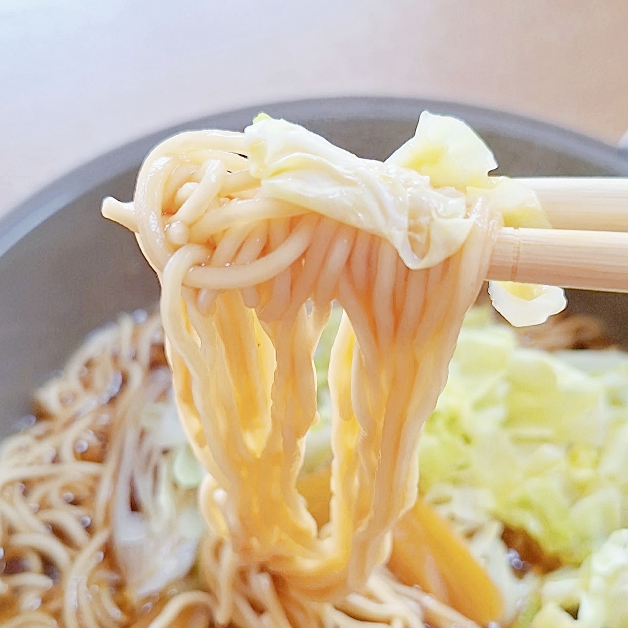 箸で持ち上げたラーメンとキャベツの具材が見える食事風景。