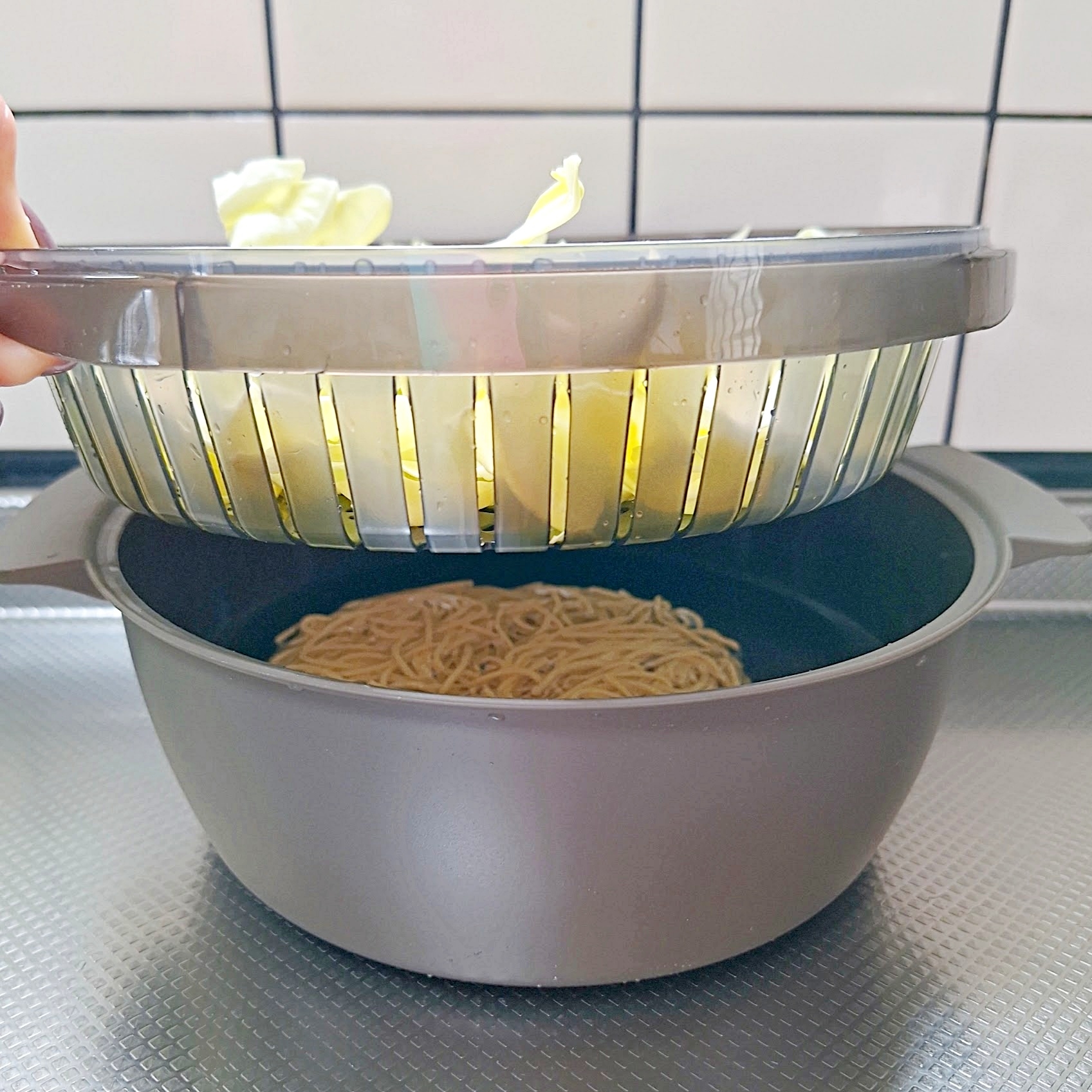 鍋の中で麺を茹でる様子、手がふたを持ち上げキャベツを見せている。