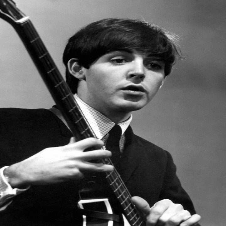 A musician plays a guitar on stage, dressed in a classic suit and tie, focused on his performance