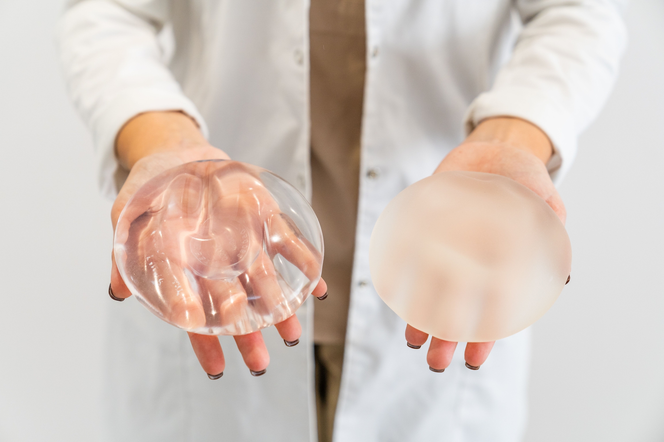 Person i laboratoriefrakk som holder to brystimplantater, en silikon og en saltvann, og viser forskjellene i materiale