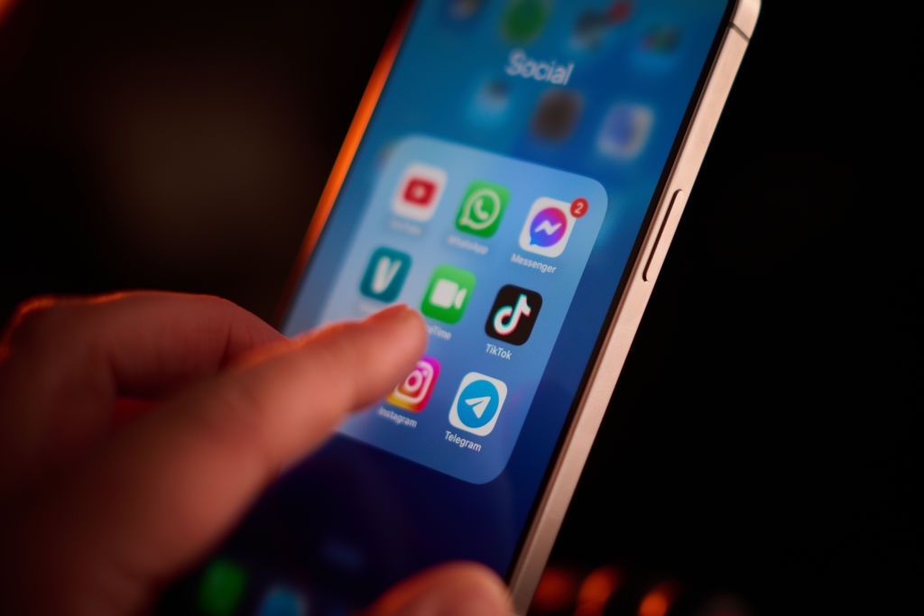 Fingre tapper på en smarttelefonskjerm som viser appikoner på sosiale medier, inkludert YouTube, WhatsApp, Tiktok og Instagram