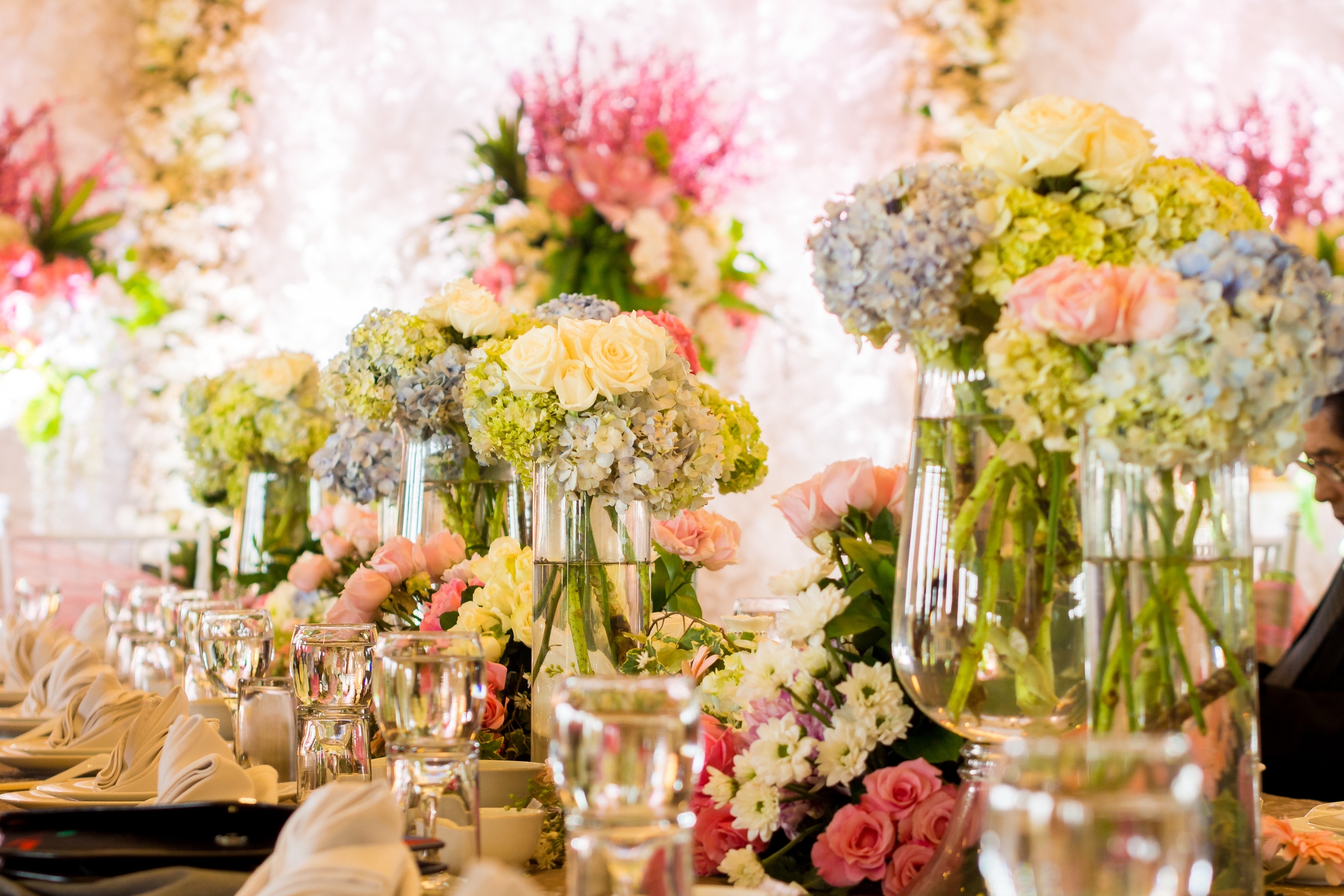 Elegant bordinnstilling med blomster midtstykker, inkludert hortensiaer og roser, omgitt av pent anordnet glass og servietter