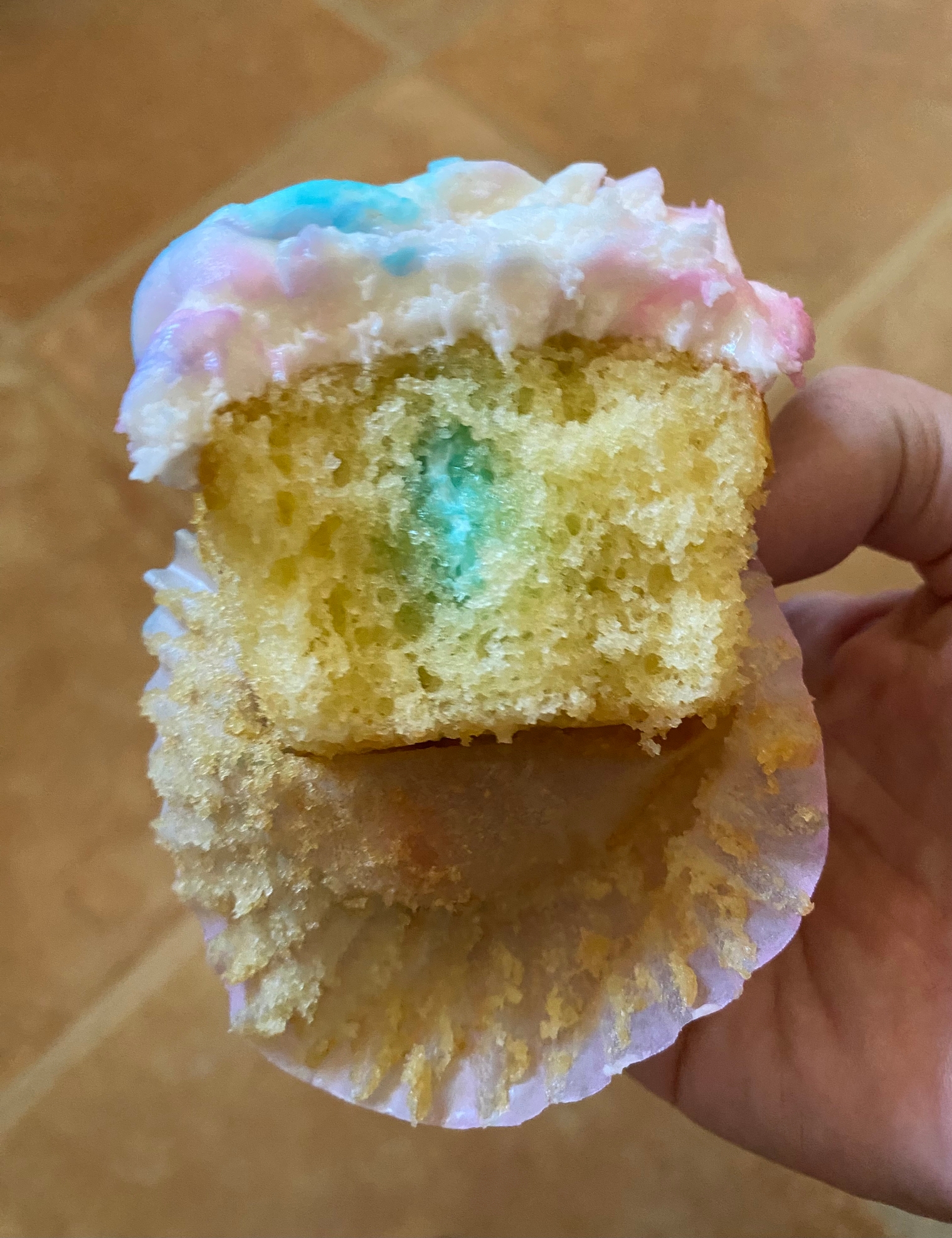 En person som holder en delvis skrellet cupcake med flerfarget frosting og en bit tatt ut, og avslører et fuktig interiør med et tonet senter
