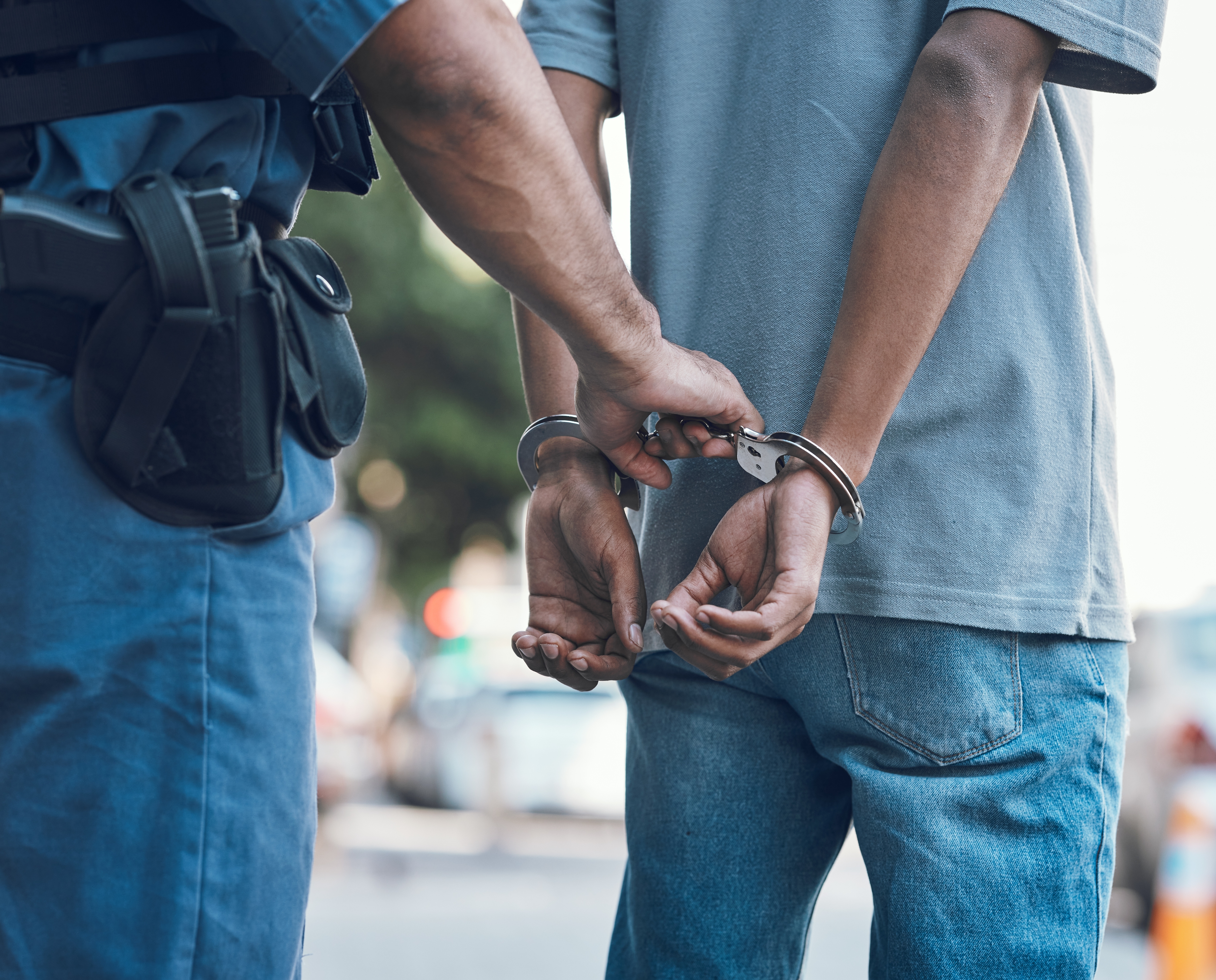 A police officer handcuffs a person's hands behind their back during an arrest on the street
