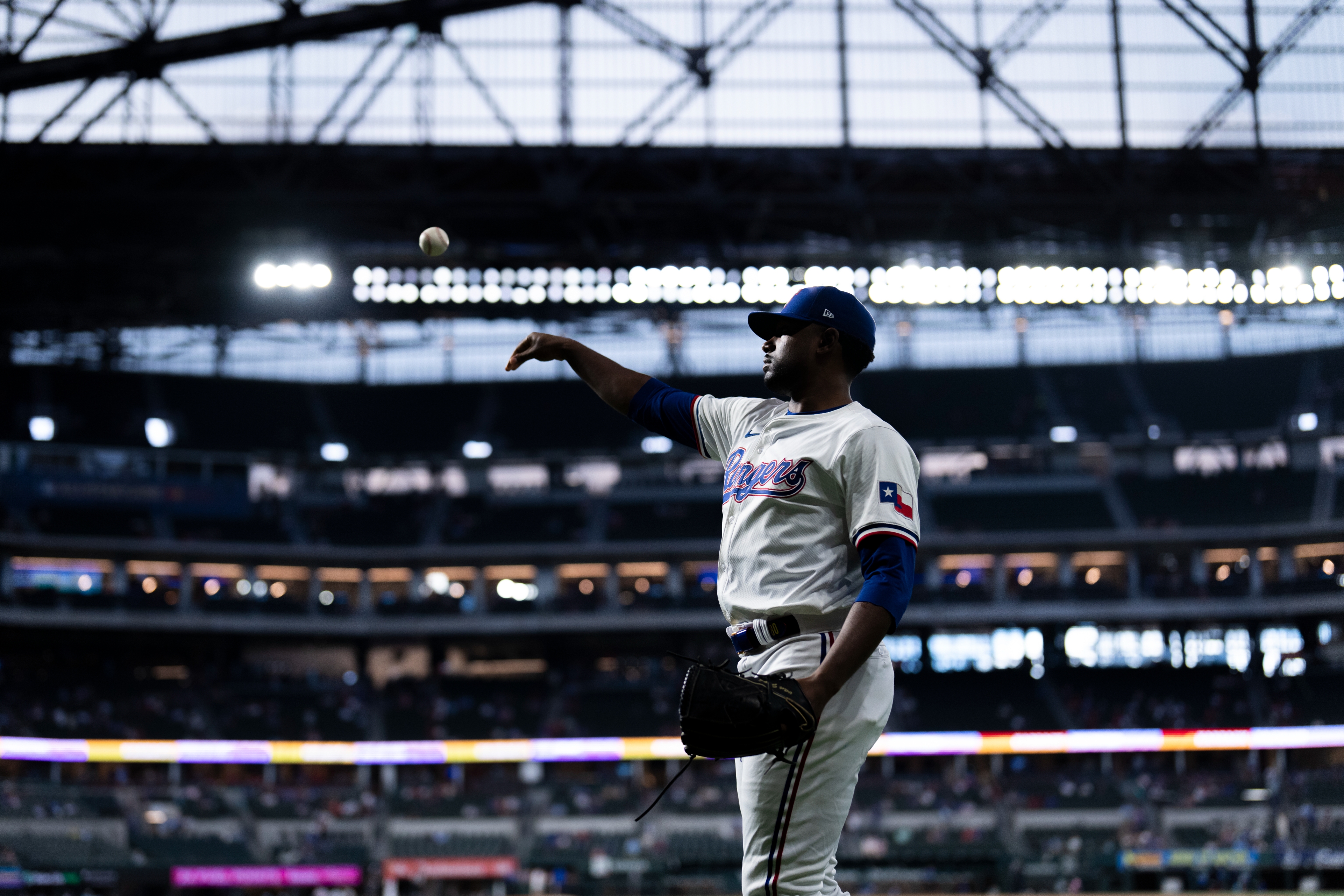 Baseball player in mid-pitch during a game, stadium lights in the background, wearing a uniform with a team logo