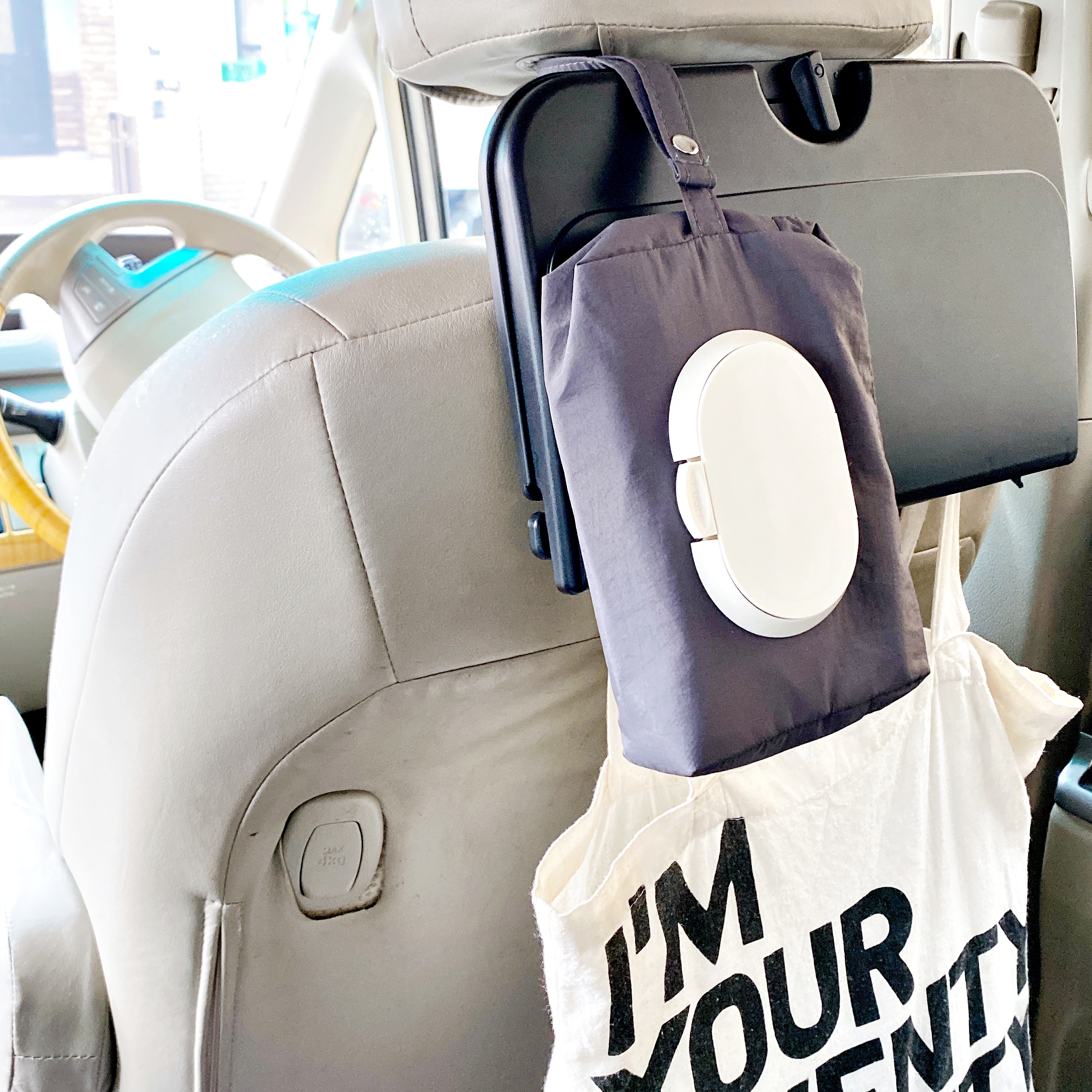 車の座席の後ろに取り付けられた折りたたみテーブルと収納バッグ。バッグの隣に「I'M YOUR MOMMY」と書かれたバッグが吊るされている。