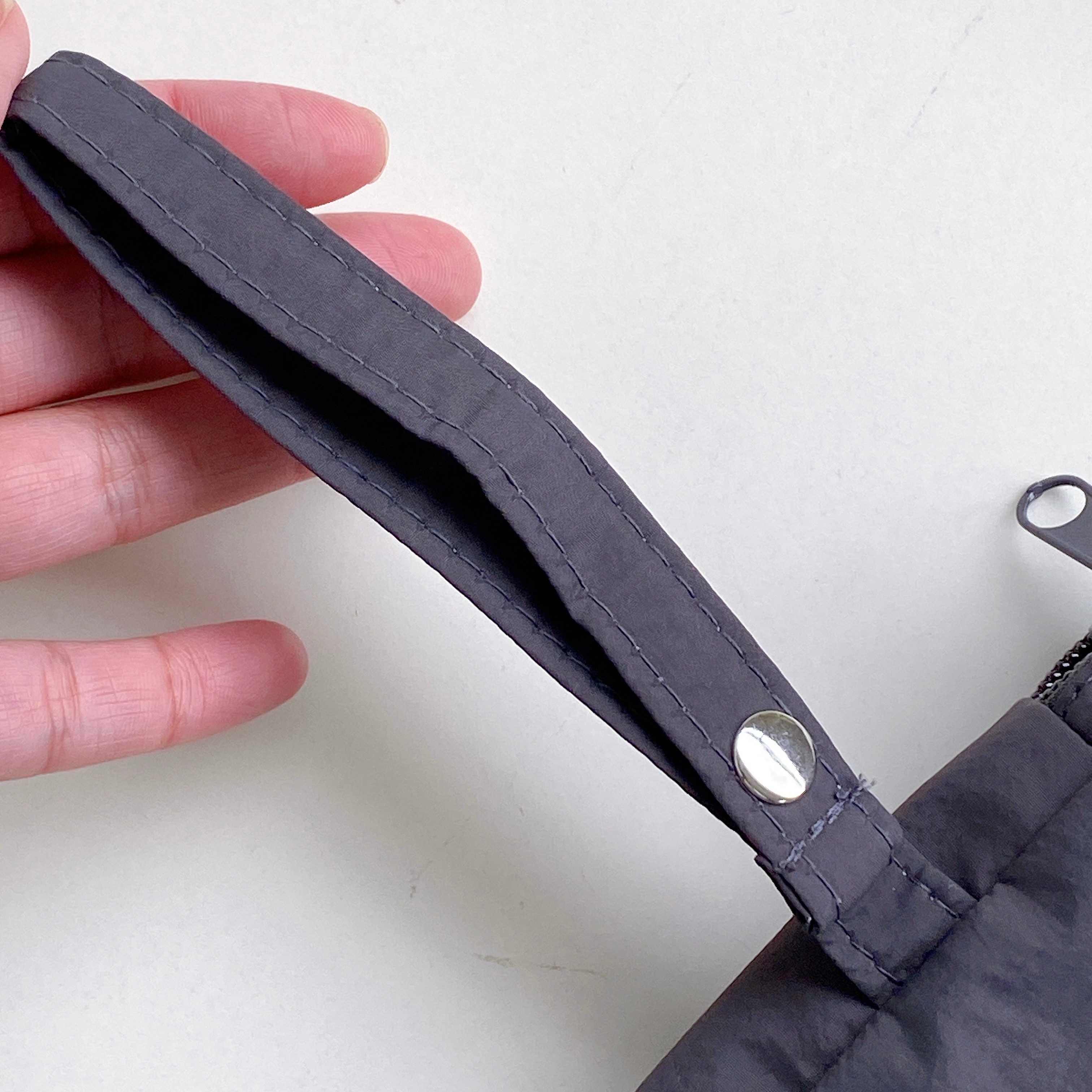 手で持っている小さな黒いポーチのハンドル部分がクローズアップされた写真。ロゴボタンが付いています。