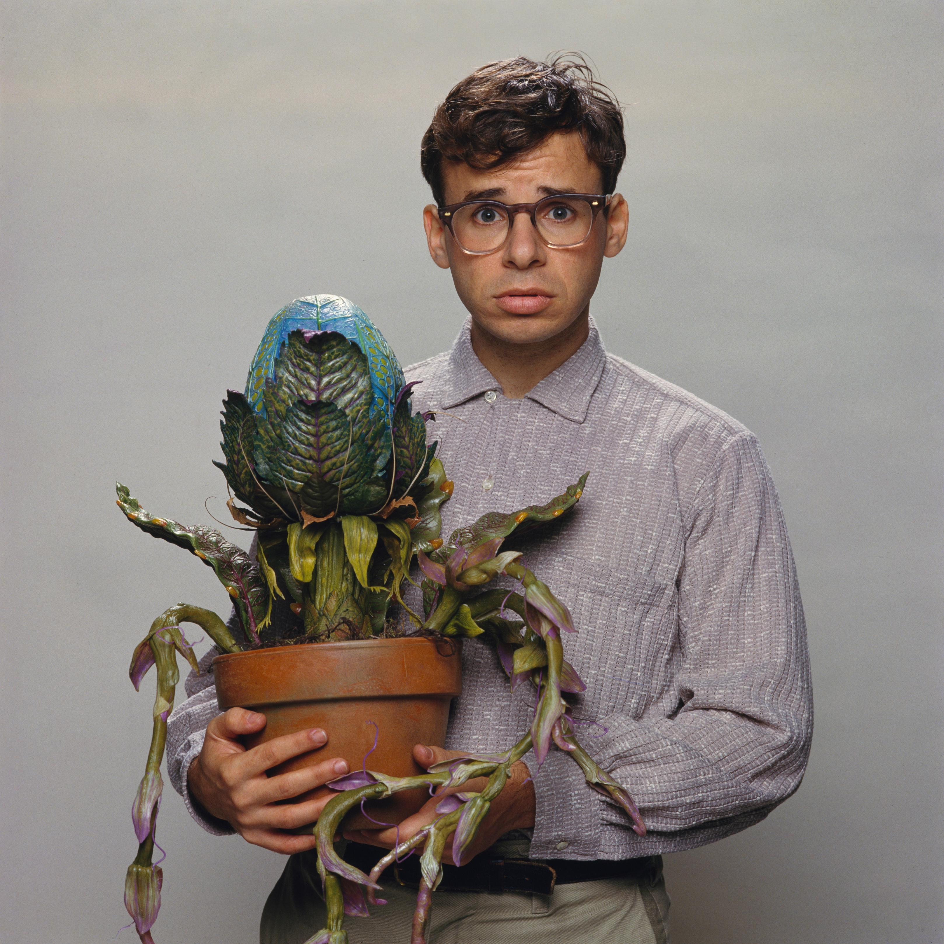 Person holding a large, unusual potted plant with wide eyes and a concerned expression