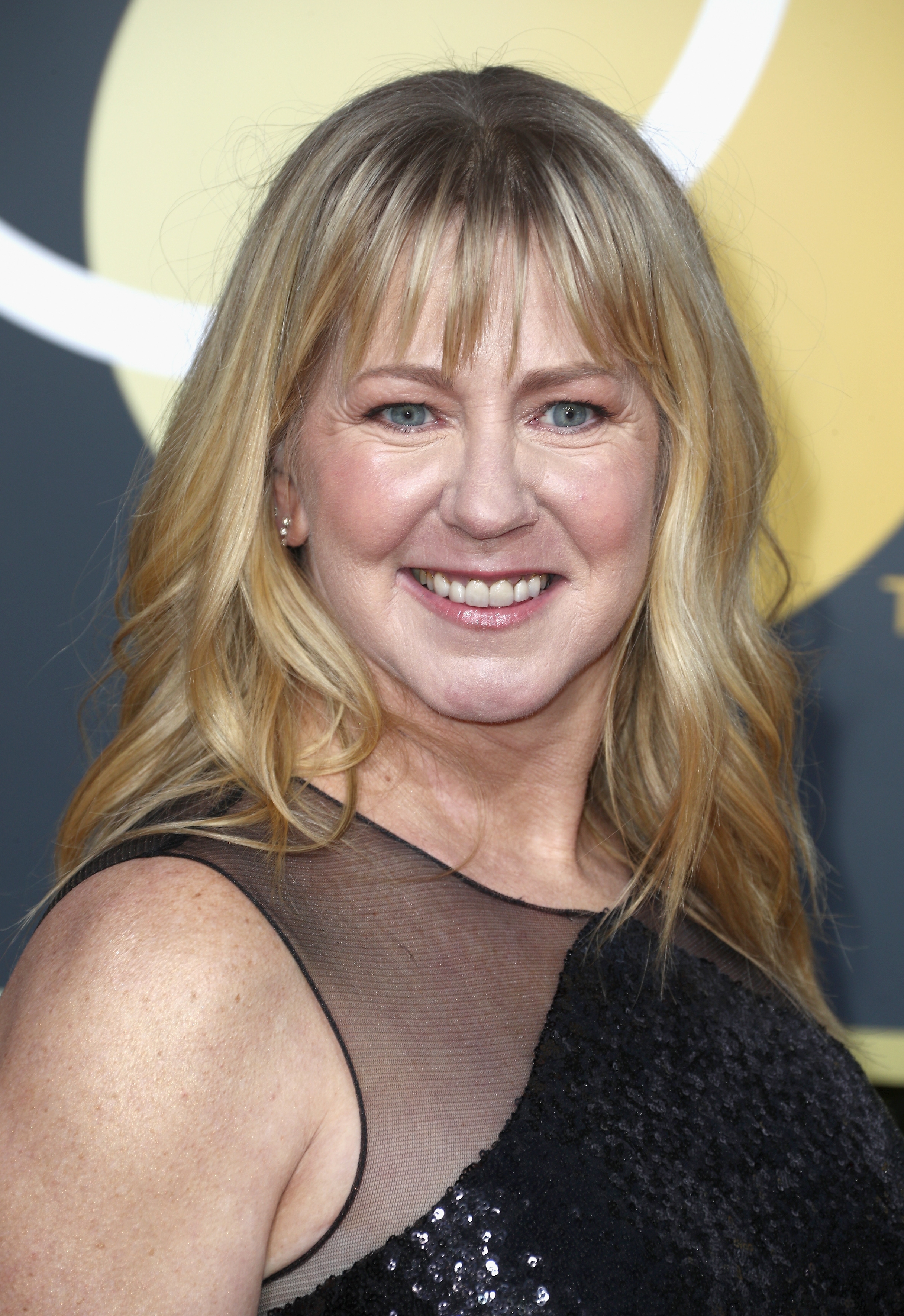 Person on a red carpet wearing a sleeveless, sequined dress with sheer detailing, smiling at the camera