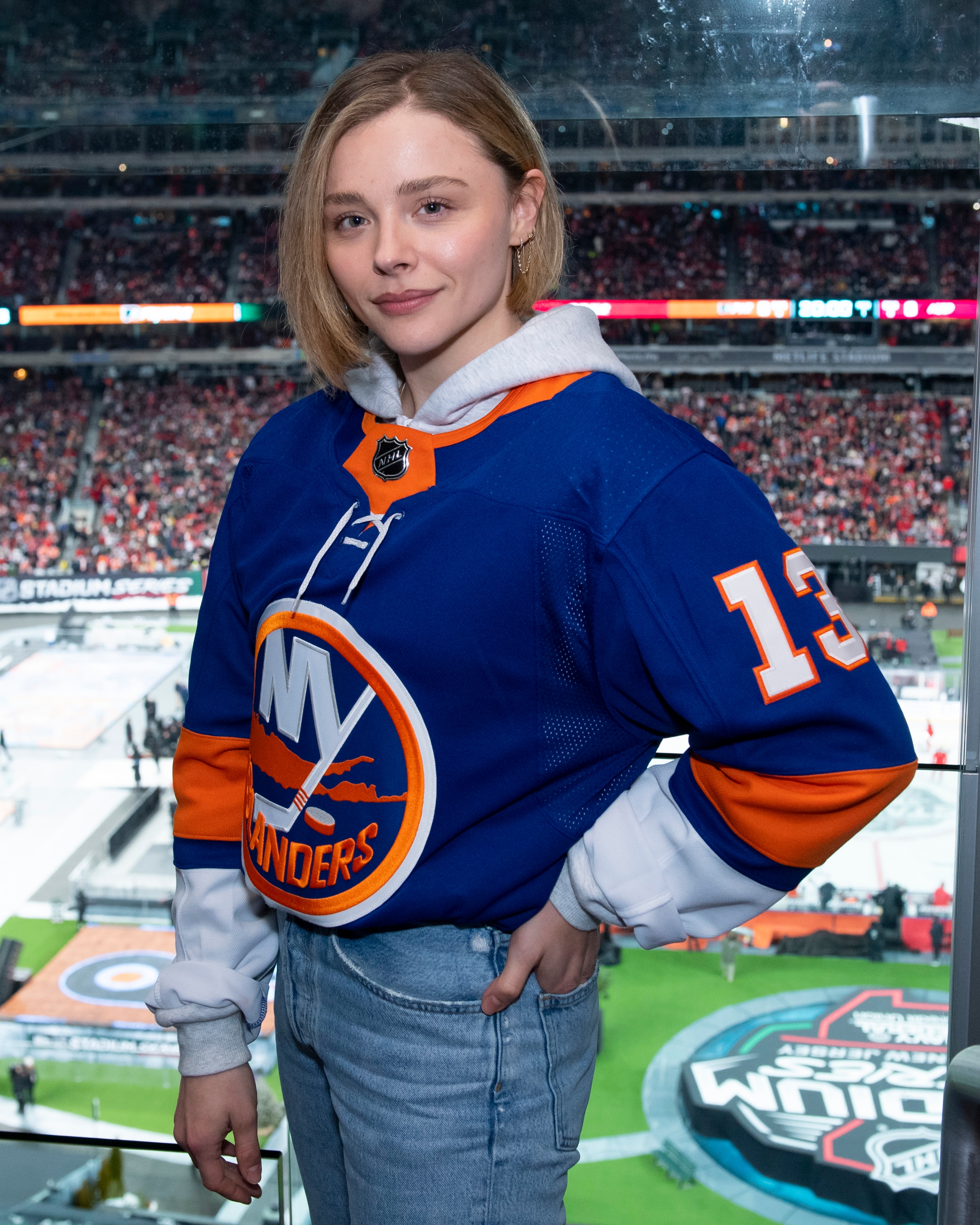 Person wearing a hockey jersey at a stadium event, smiling and posing with hand on hip