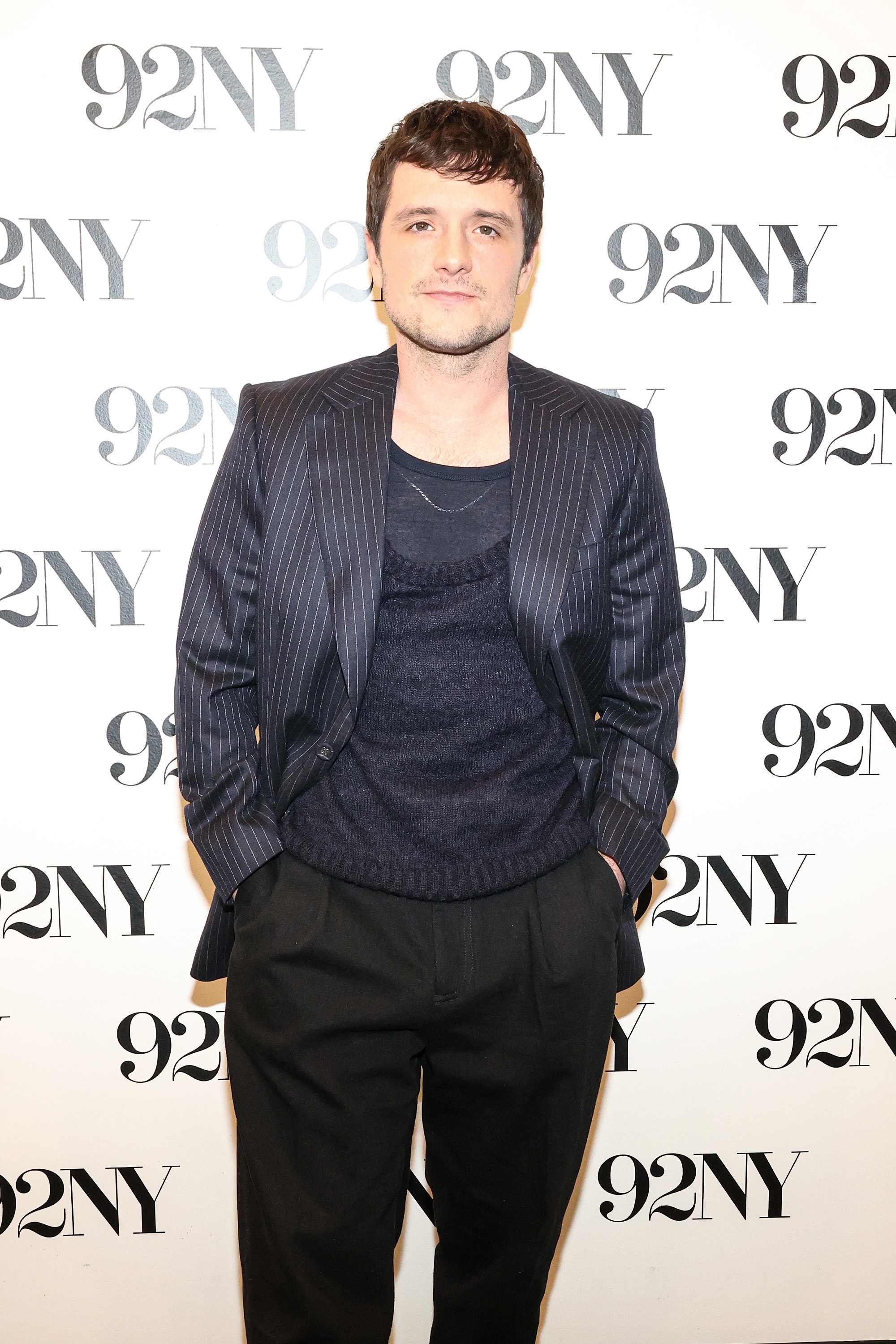 Person in a pinstripe suit and sweater poses at a 92NY event backdrop