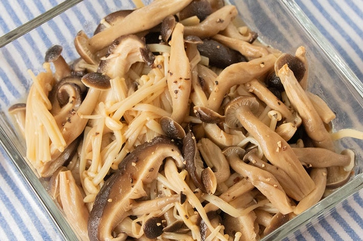 ガラス皿に盛られた数種類の調理されたきのこのマリネがストライプの布の上に置かれている。