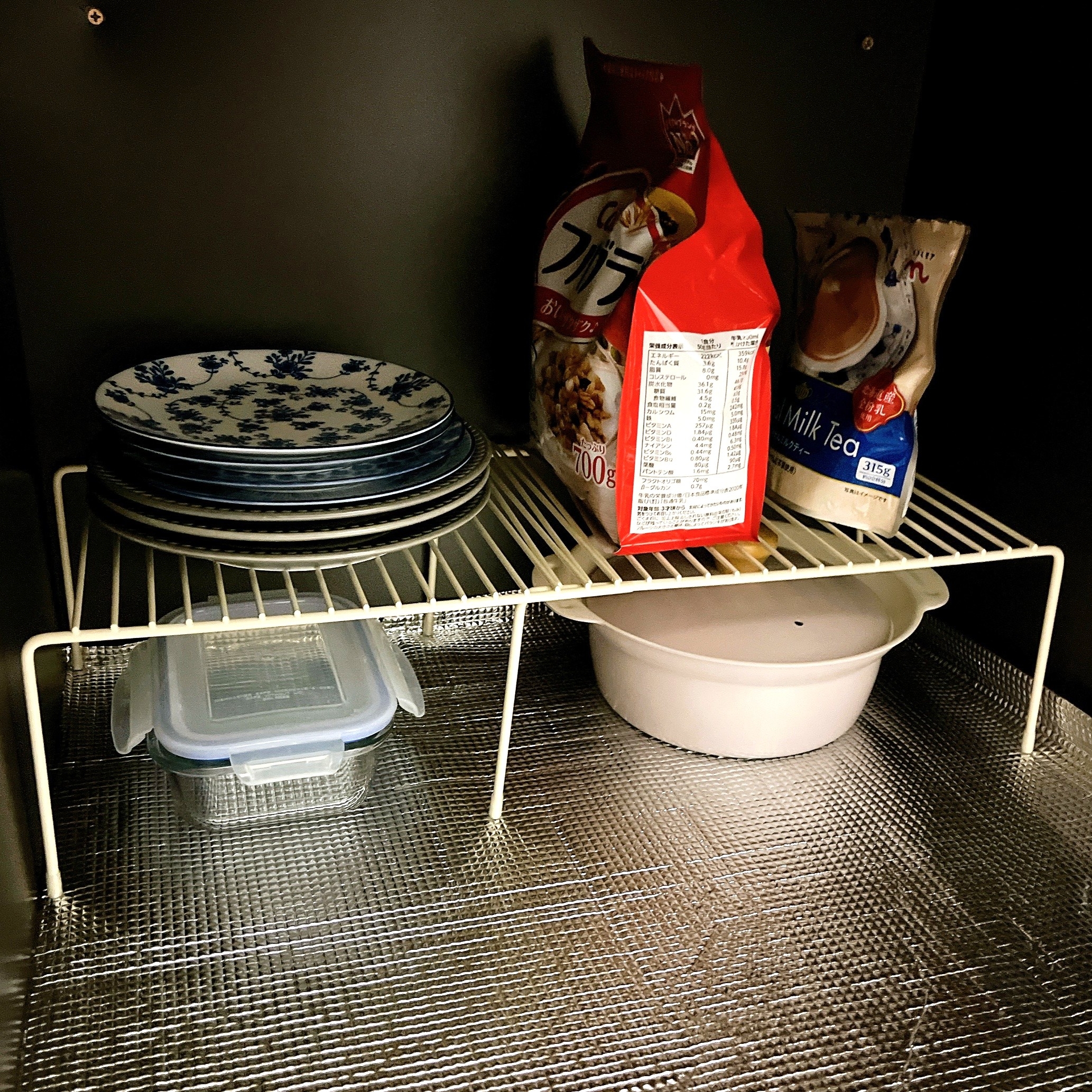 戸棚の中の棚に積まれた食器、保存容器、袋入りのお菓子。