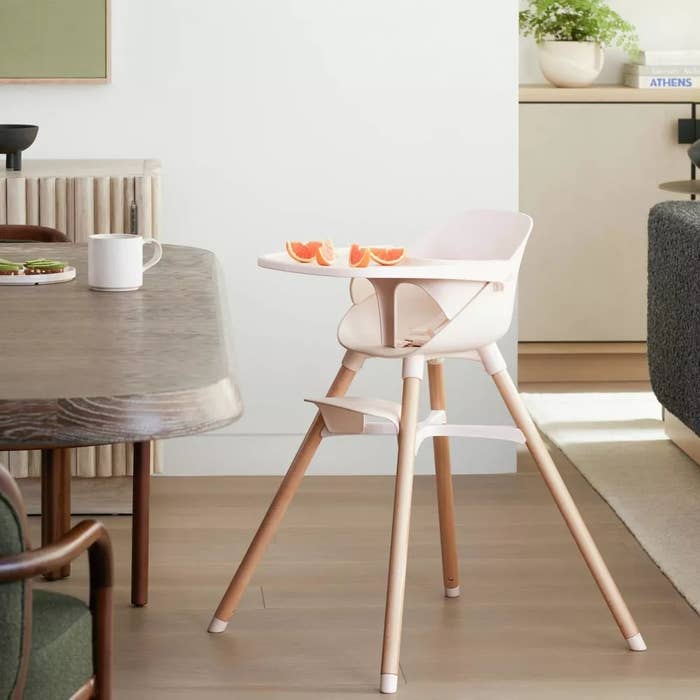 A modern precocious seat with woody legs and achromatic spot stands beside a eating table, with orangish slices connected its tray