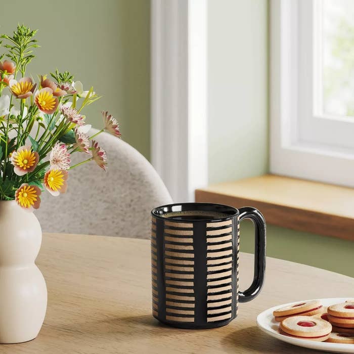 A decorative mug with a striped signifier sits connected a array adjacent flowers and cookies, by a window