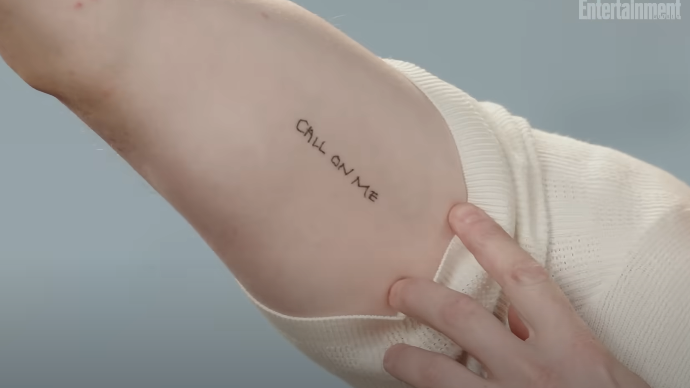 A person's arm with a tattoo reading "CALL ON ME," alongside a hand gently pulling back a shirt sleeve to reveal the design
