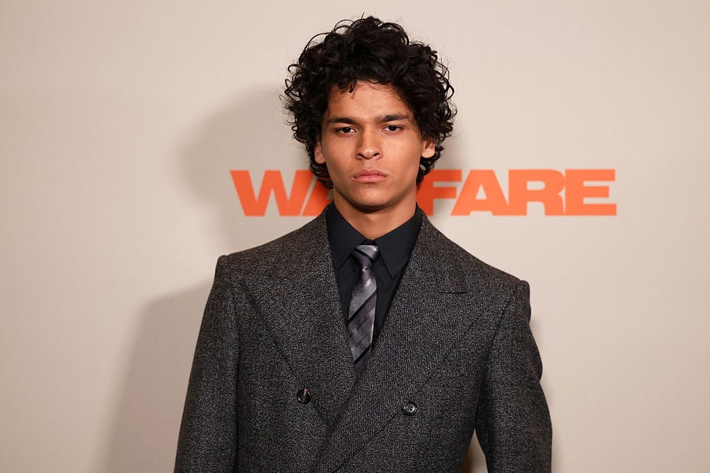 Person wearing a sharp suit with a tie, posing against a background with "Warfare" text