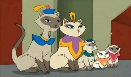 Animated cats in royal attire sit together; each wears a regal collar and headpiece, suggesting a family scene in an animated show