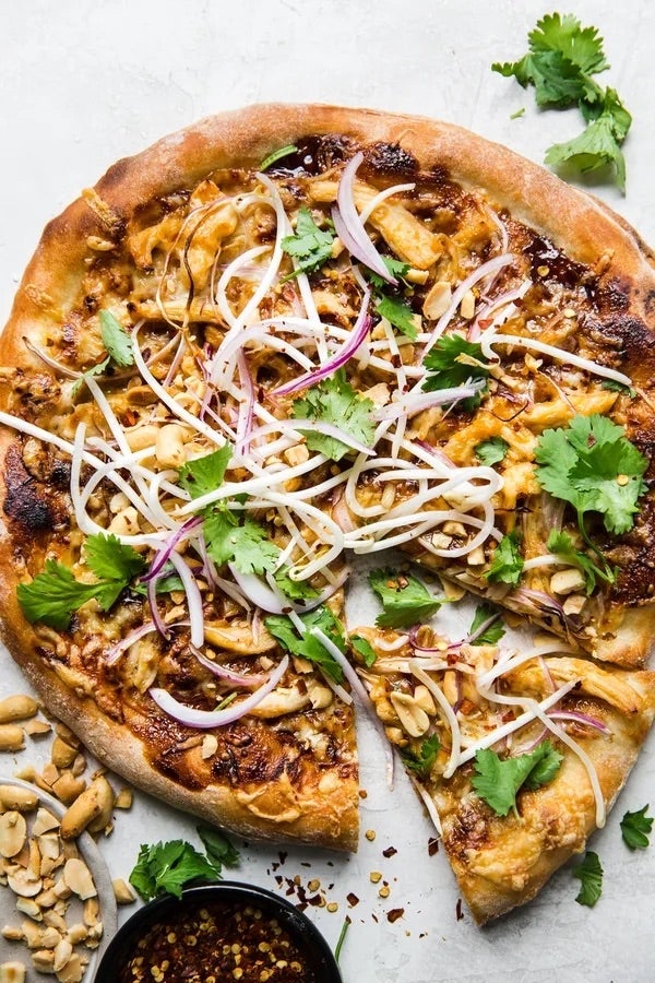 Pizza topped with bean sprouts, cilantro, sliced onions, peanuts, and a slice partially cut out