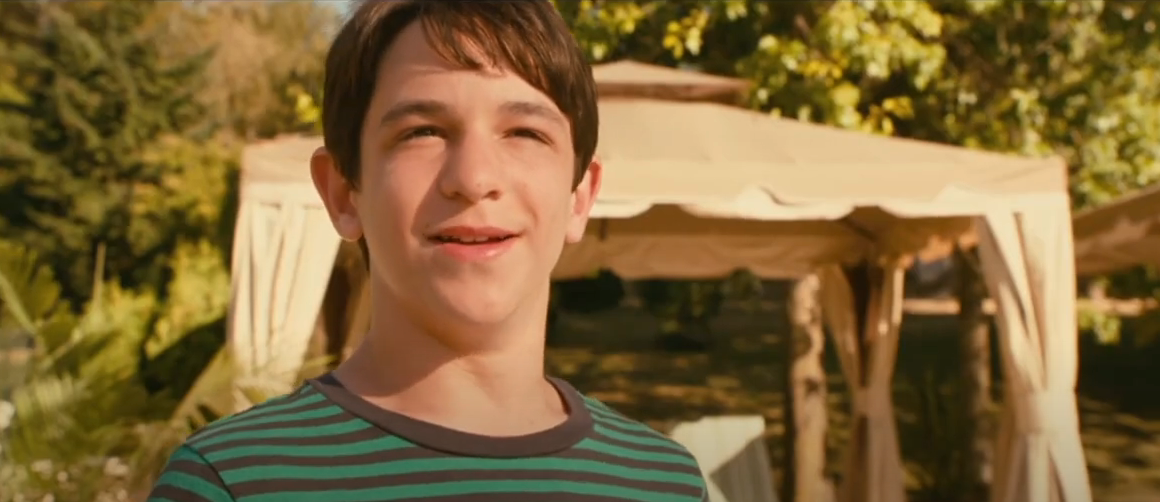 Greg Heffley in "Diary of a Wimpy Kid: Dog Days" smiling in front of a poolside cabana