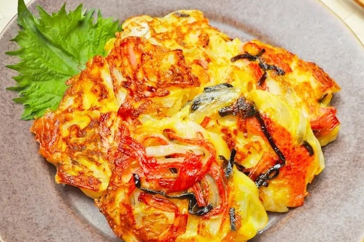 お皿に盛られた韓国風チヂミ。ネギやシーフードの具が見える。左に緑の葉が飾られている。